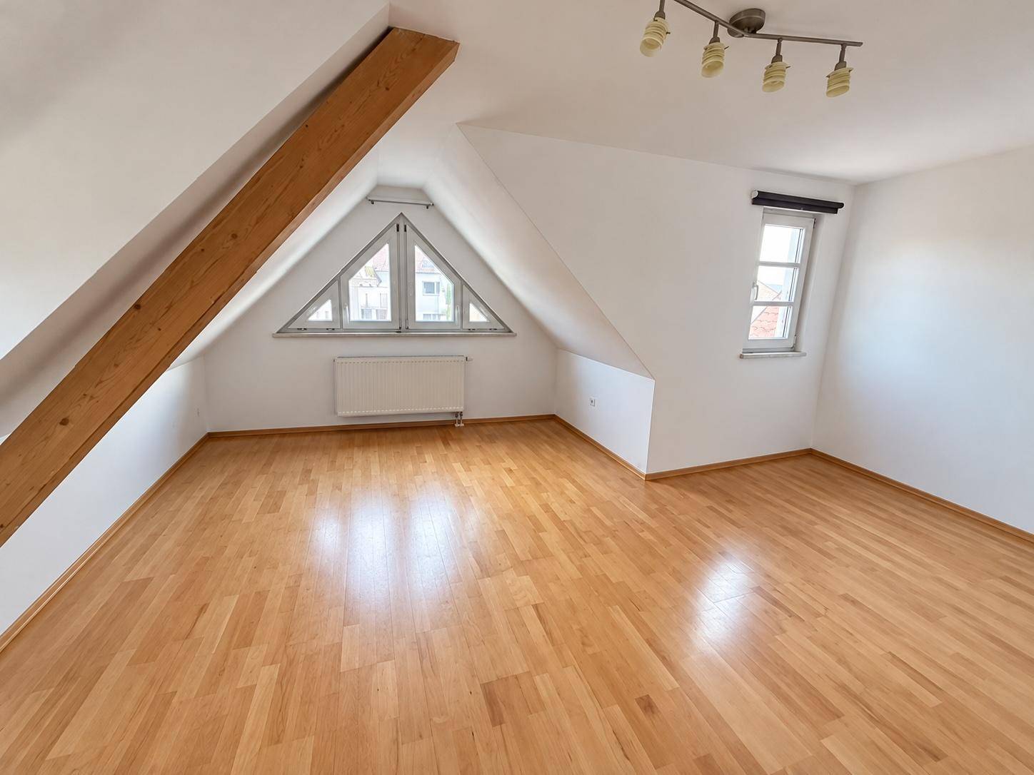 Lichtdurchflutetes Dachgeschosszimmer mit Parkettboden, Holzbalken und charakteristischen Giebelfenstern.