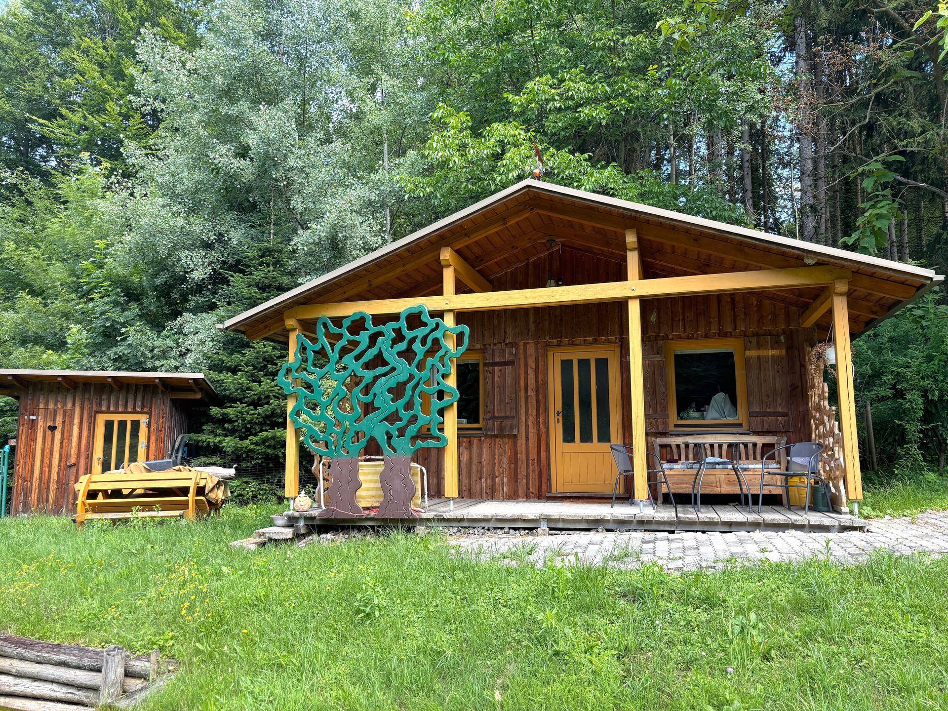 Gemütliche Holzhütte mit Veranda und Sitzgelegenheiten im Freien, neben einem kleineren Schuppen.