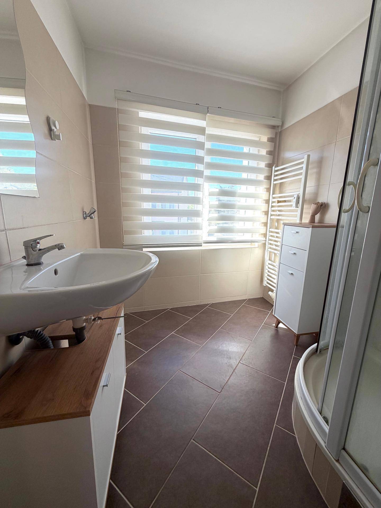 Modernes Badezimmer mit Waschbecken, Spiegelschrank und beigefarbenen Fliesen.