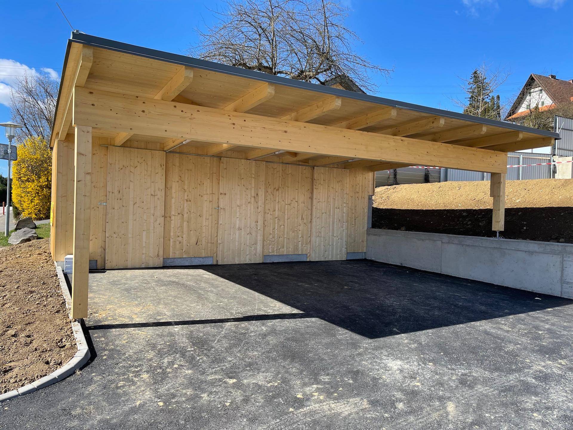 Moderner Holz-Carport mit asphaltierter Zufahrt, bietet geschützten Parkraum.