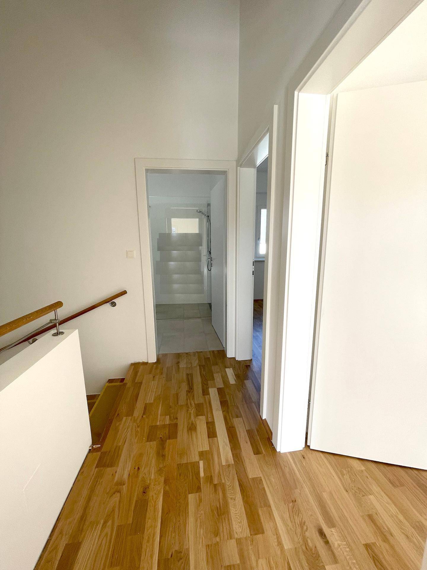 Oberer Flur mit Holzfußboden, der zu weiteren hellen Zimmern und dem Badezimmer führt.
