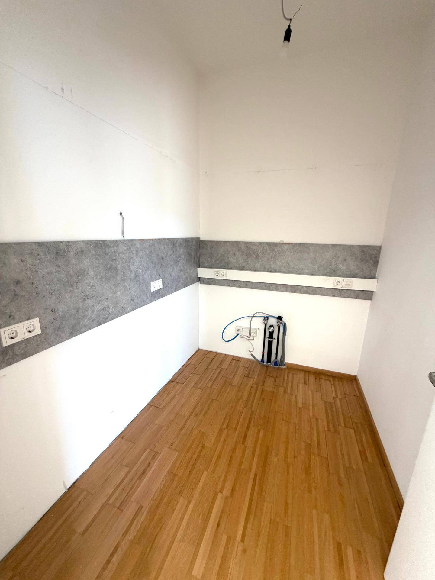Kleiner Raum mit Holzfußboden, weißen Wänden und Anschlüssen für technische Geräte.
