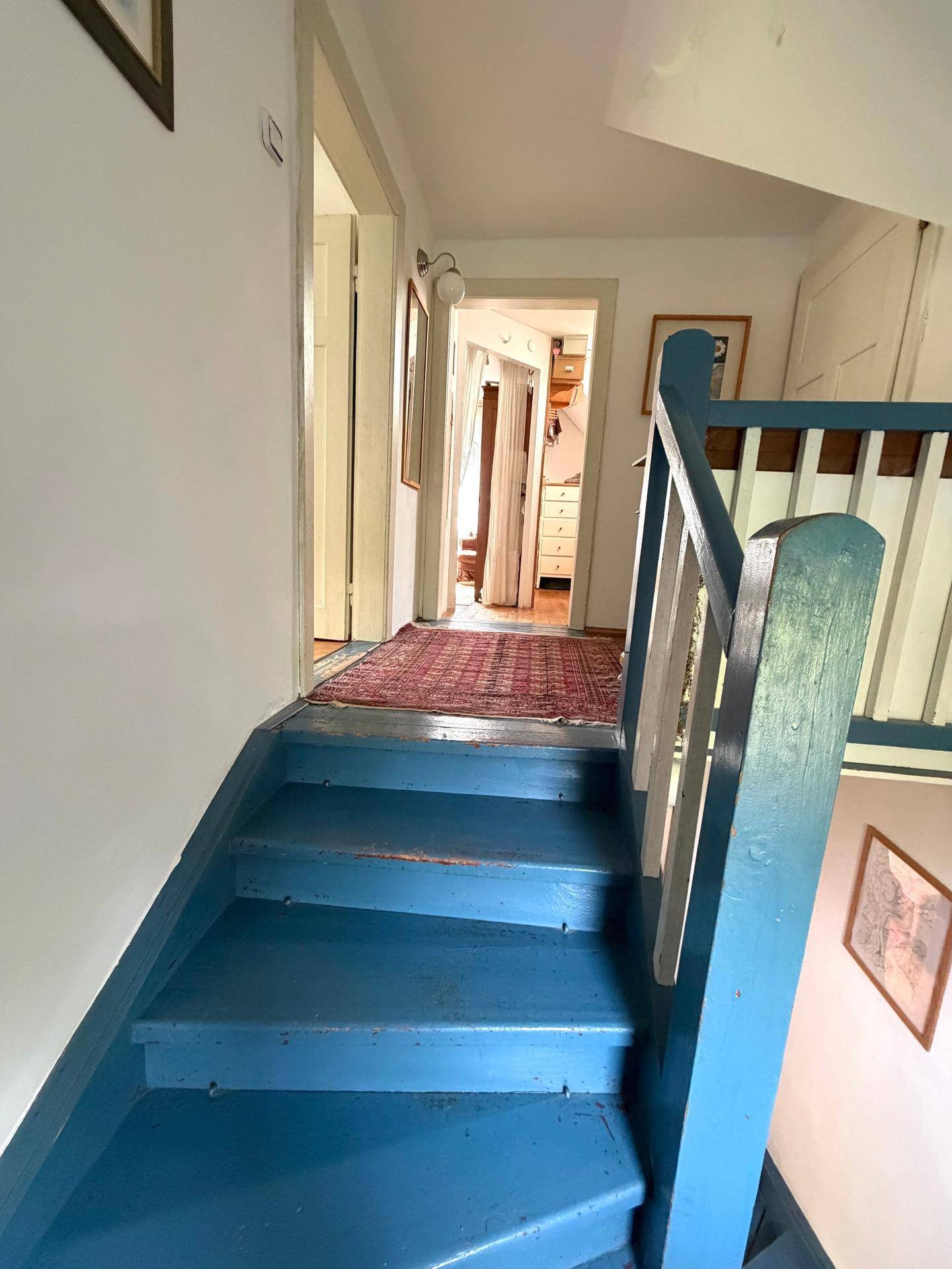 Blaue Holztreppe führt zu einem Flur mit Teppich und weiteren Zimmern.