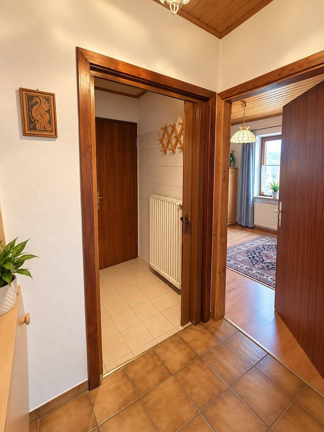 Flur mit Fliesenboden und Holztüren, der den Zugang zu einem Badezimmer und einem Schlafzimmer ermöglicht.