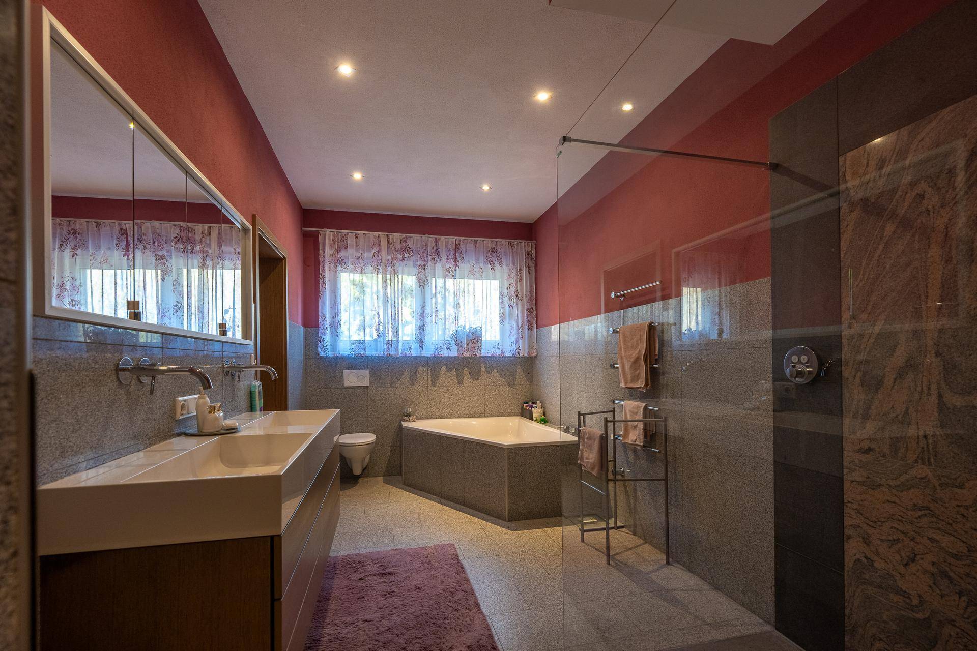 Geräumiges Badezimmer mit Doppelwaschbecken, Badewanne, Dusche und großen Fenstern.