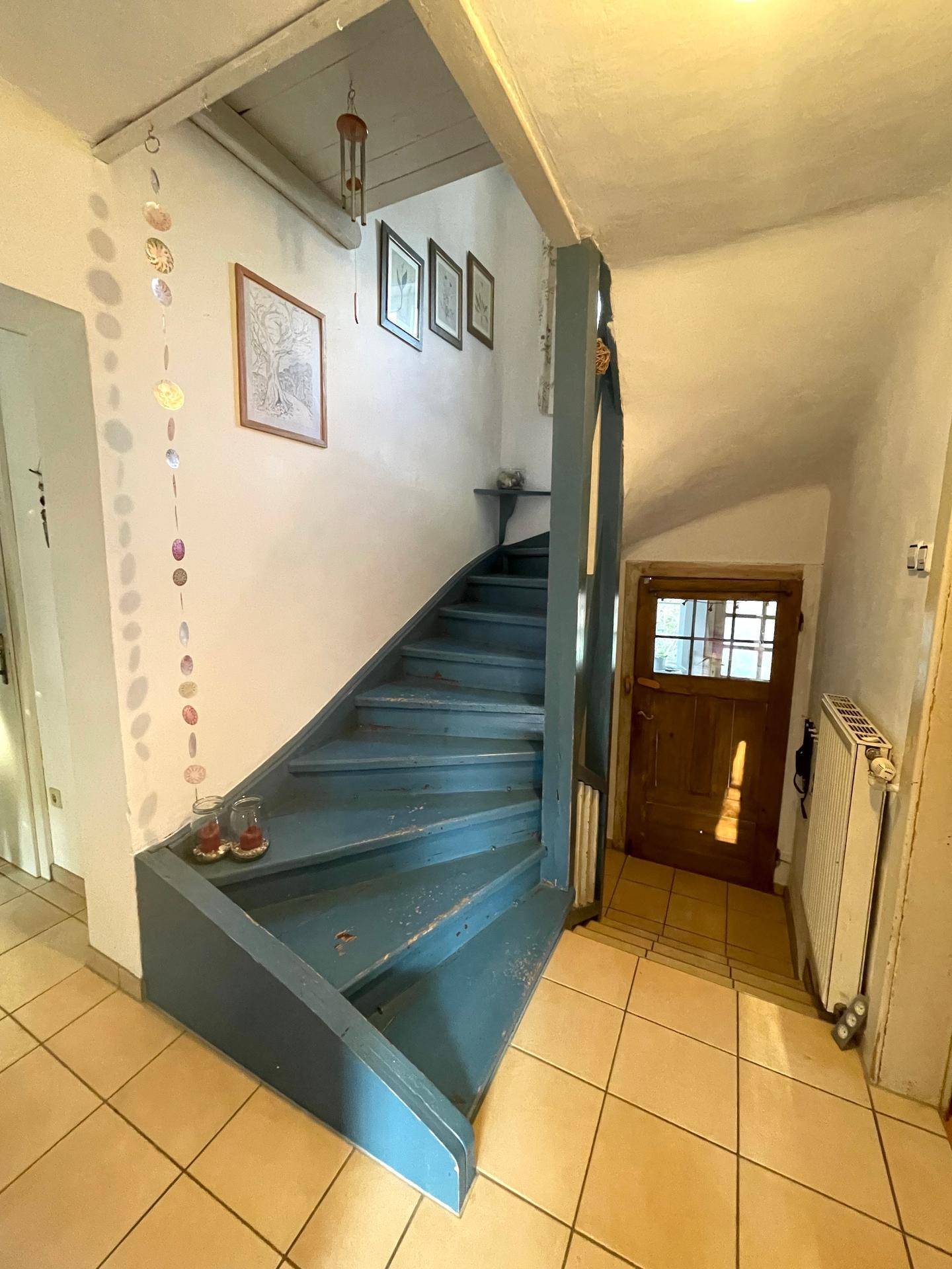 Treppenhaus mit blauer Holztreppe und Fliesenboden, führt in die oberen Etagen.