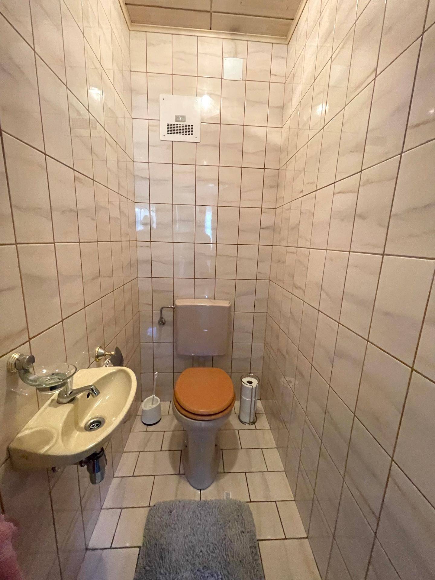 Eine kleine Gästetoilette mit hellen Fliesen, WC und Handwaschbecken.