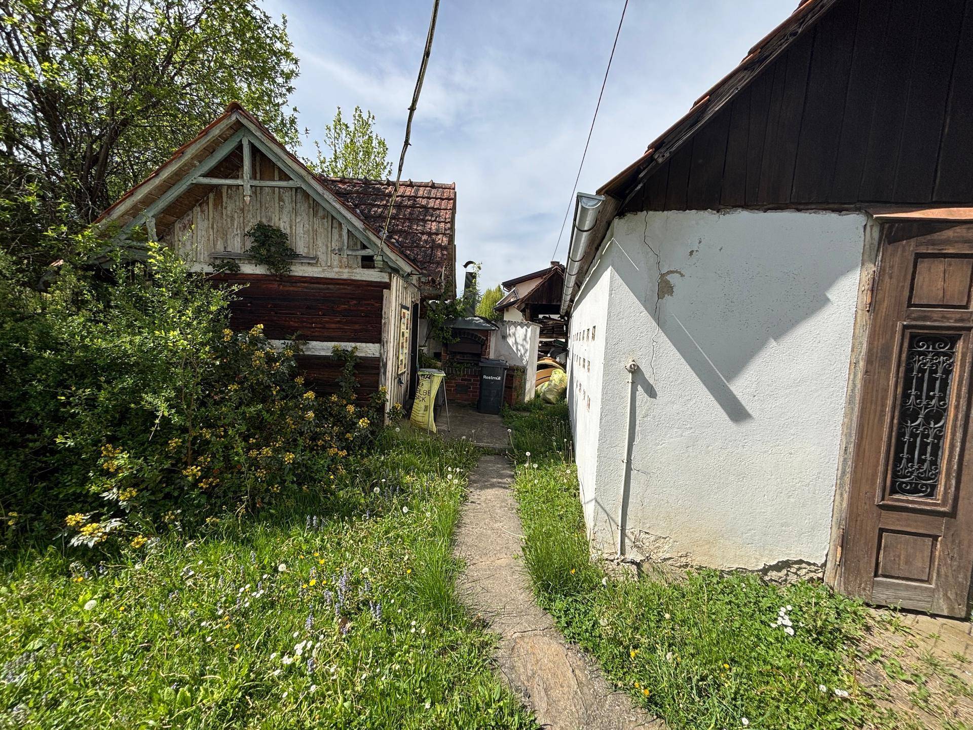 Schmaler Pfad zwischen zwei älteren Nebengebäuden, umgeben von üppiger Vegetation.