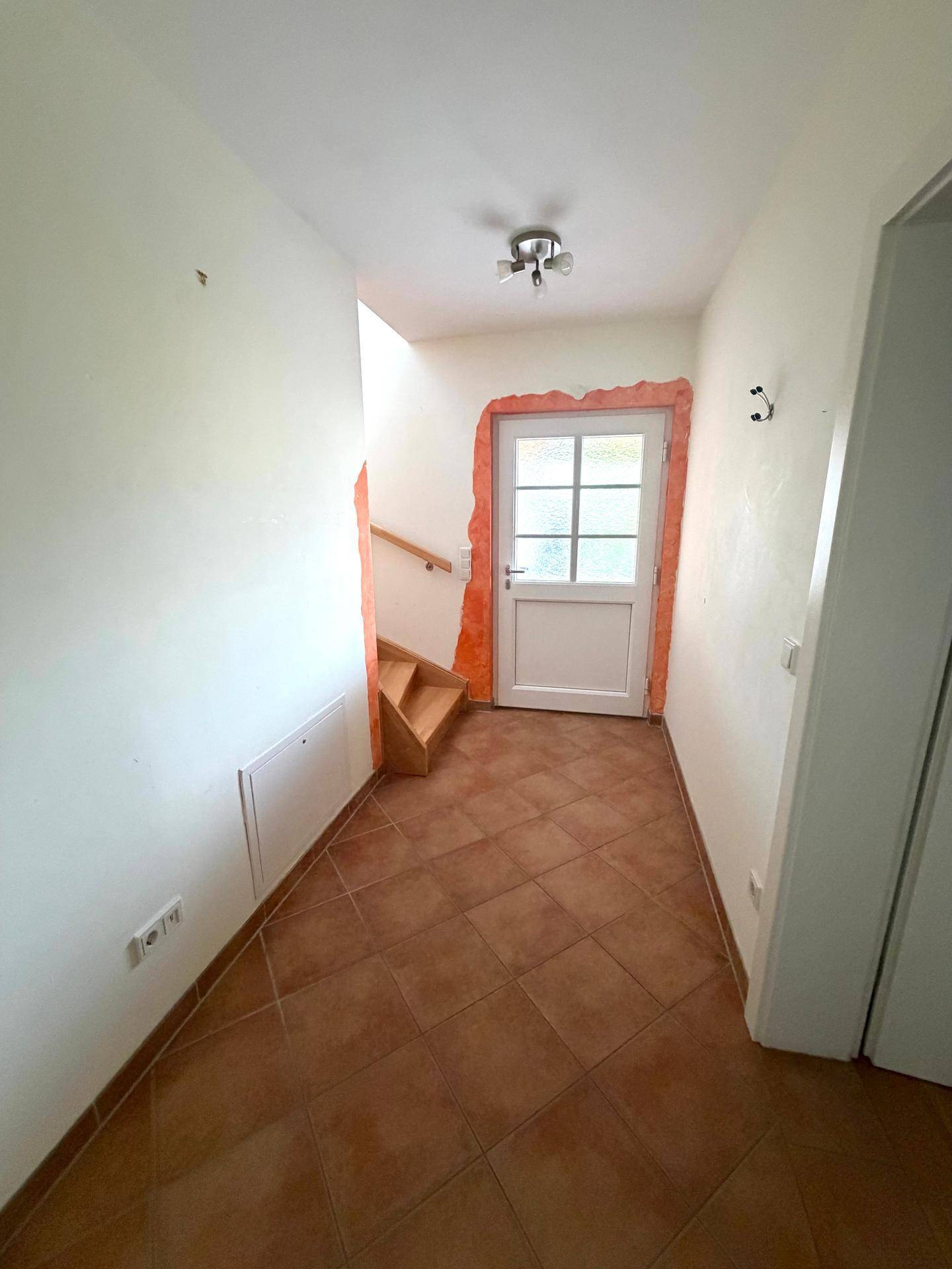 Eingangsbereich mit Terrakottafliesen und Holztreppe, die in das obere Stockwerk führt.