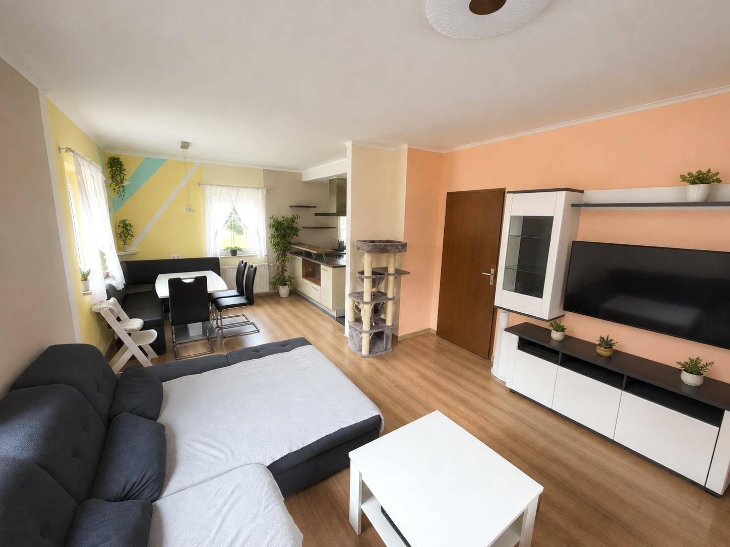 Offener Wohn- und Essbereich mit Laminatboden, Sofa und Fernsehmöbeln, verbunden mit der Küche.