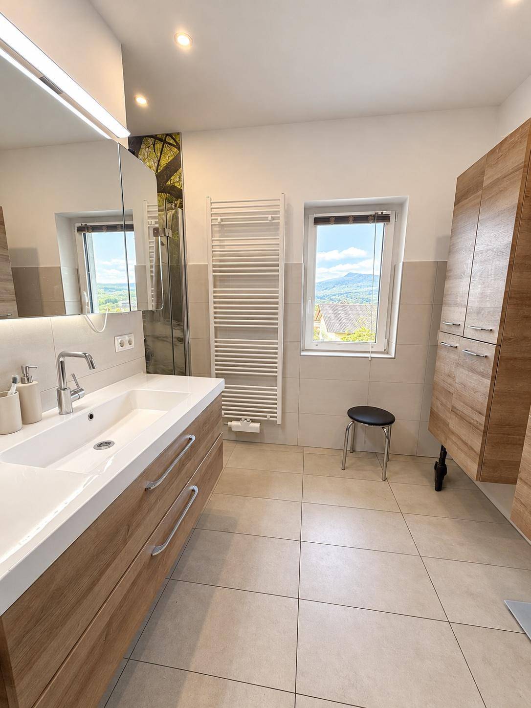 Modernes Badezimmer mit großem Waschtisch, Dusche und Fenster mit Bergblick.