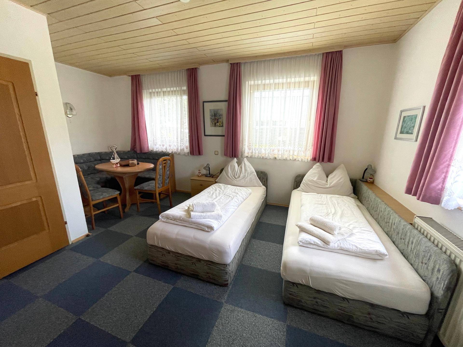 Gemütliches Schlafzimmer mit zwei Einzelbetten, einer Essecke und Teppichboden.