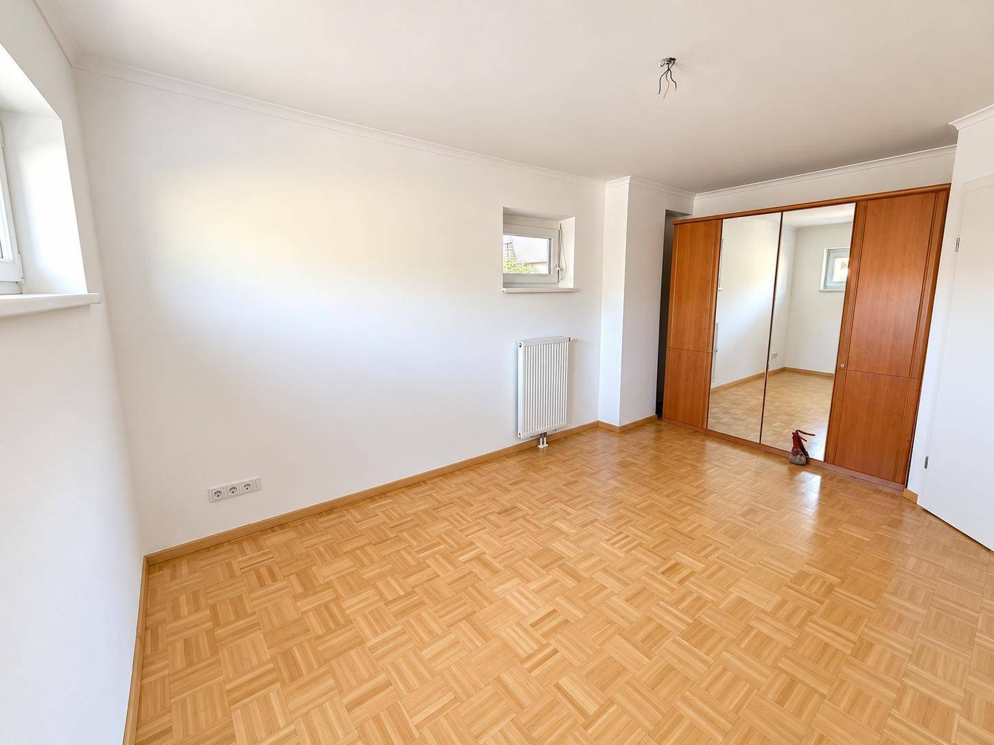 Geräumiges Schlafzimmer mit Parkettboden und einem großen Spiegelschrank.