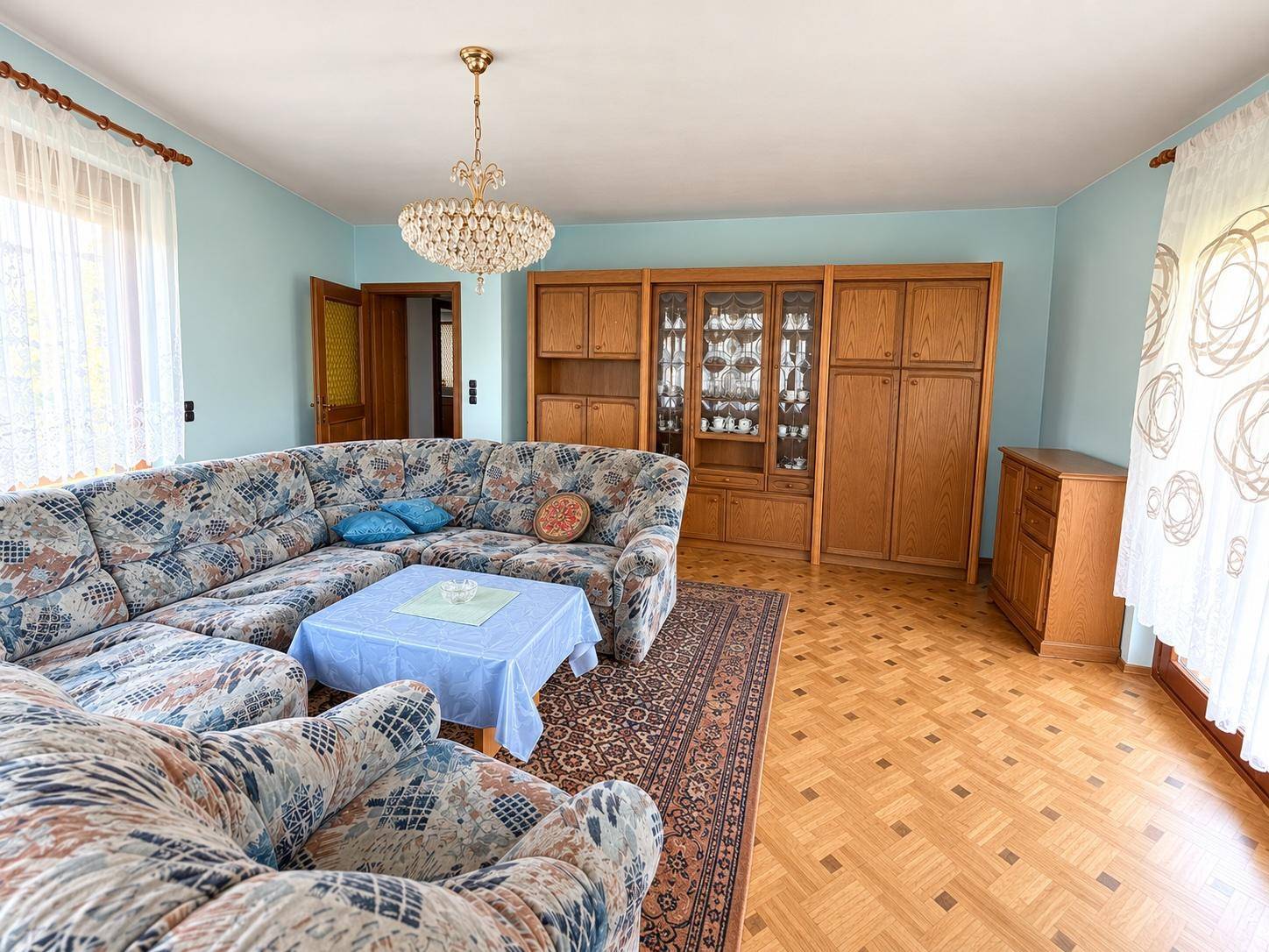 Geräumiges Wohnzimmer mit Parkettboden, großem Sofa und Schrankwand aus Holz.