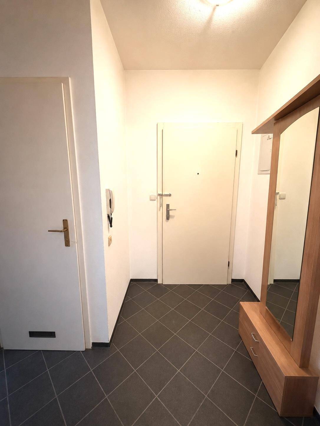 Heller Eingangsbereich mit dunklem Fliesenboden und Garderobenspiegel.