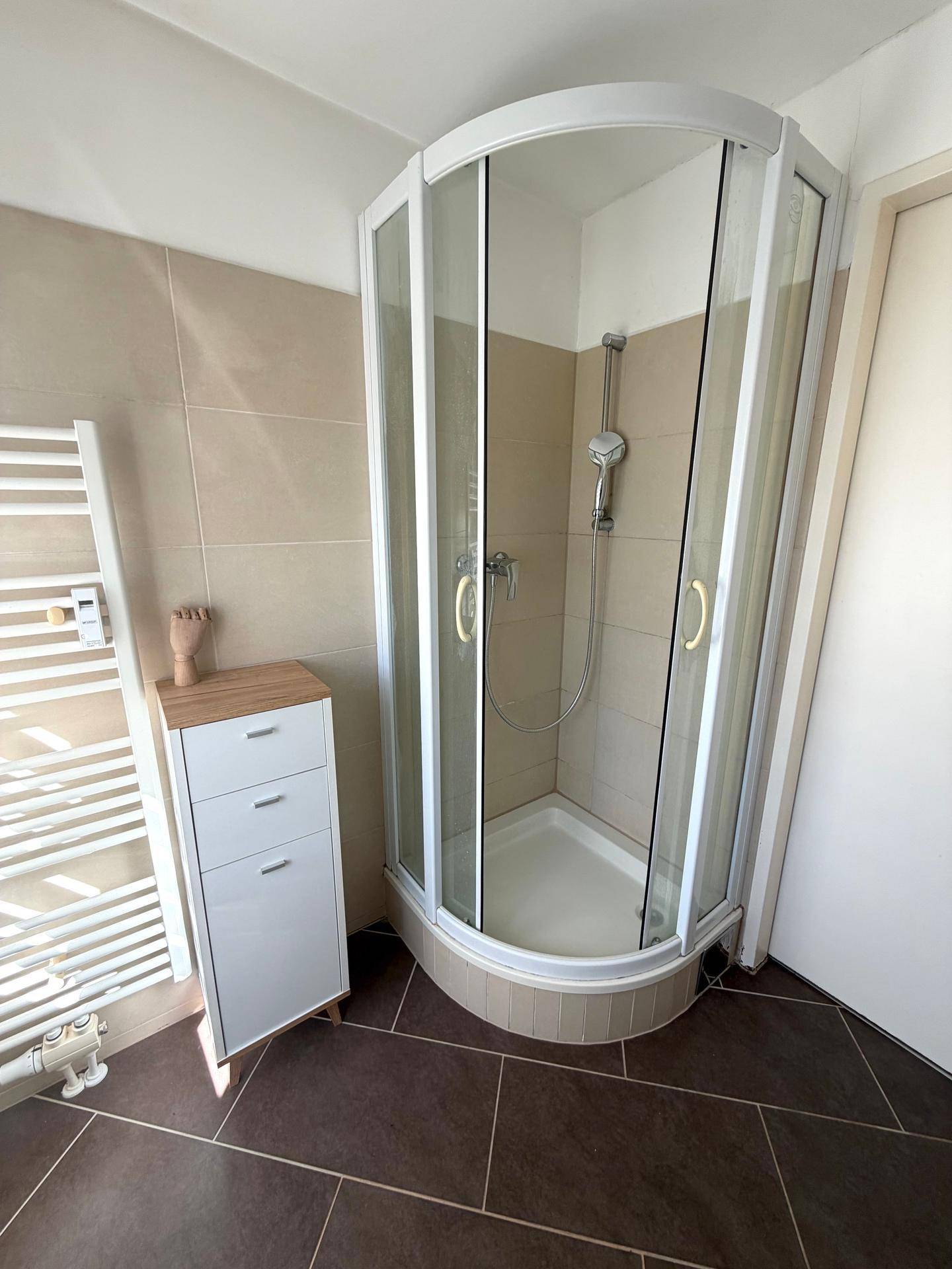 Badezimmer mit Eckdusche, beigefarbenen Fliesen und einem beheizten Handtuchhalter.