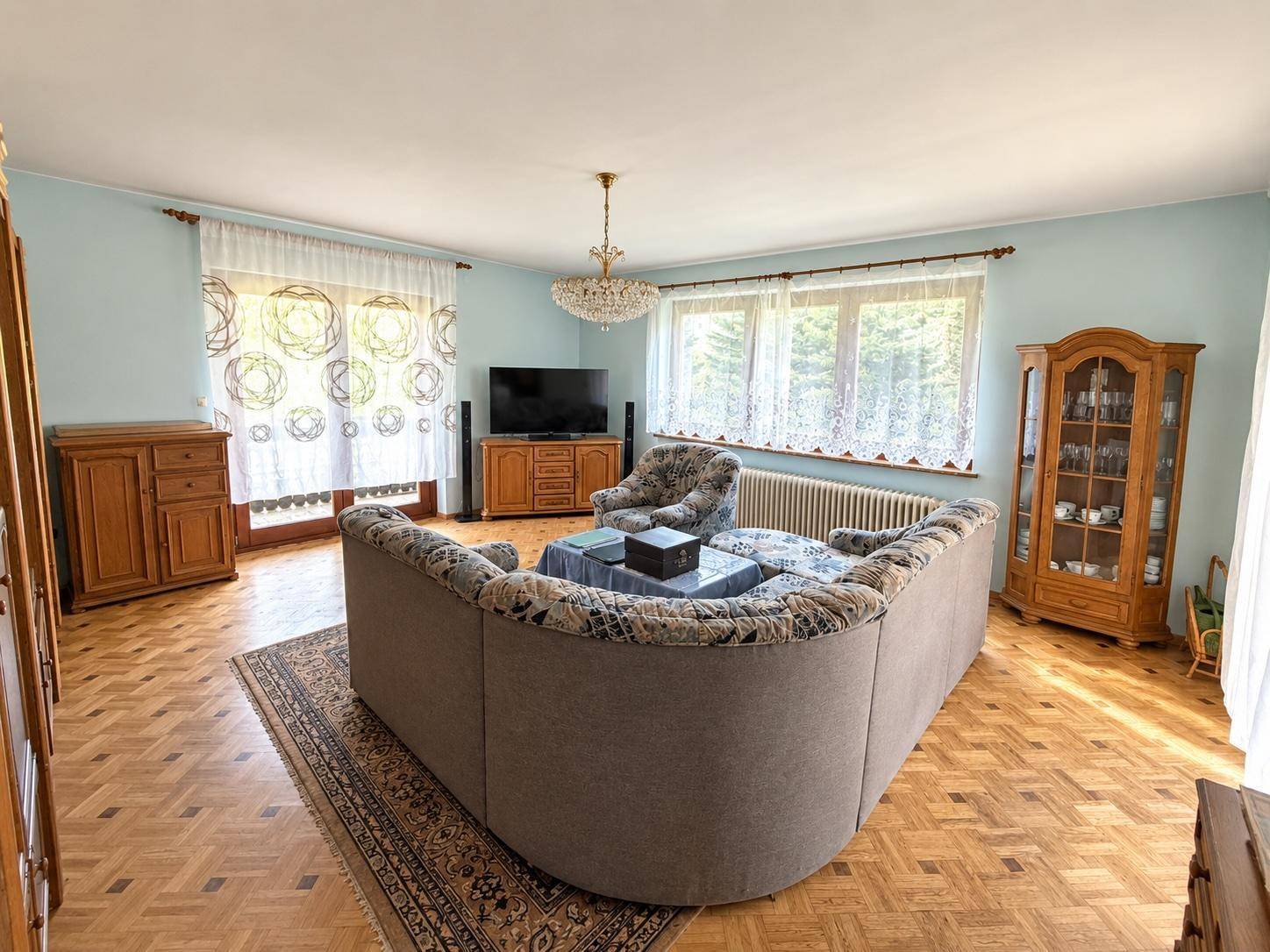 Gemütliches Wohnzimmer mit Parkettboden, großem Sofa und Blick in den grünen Garten.