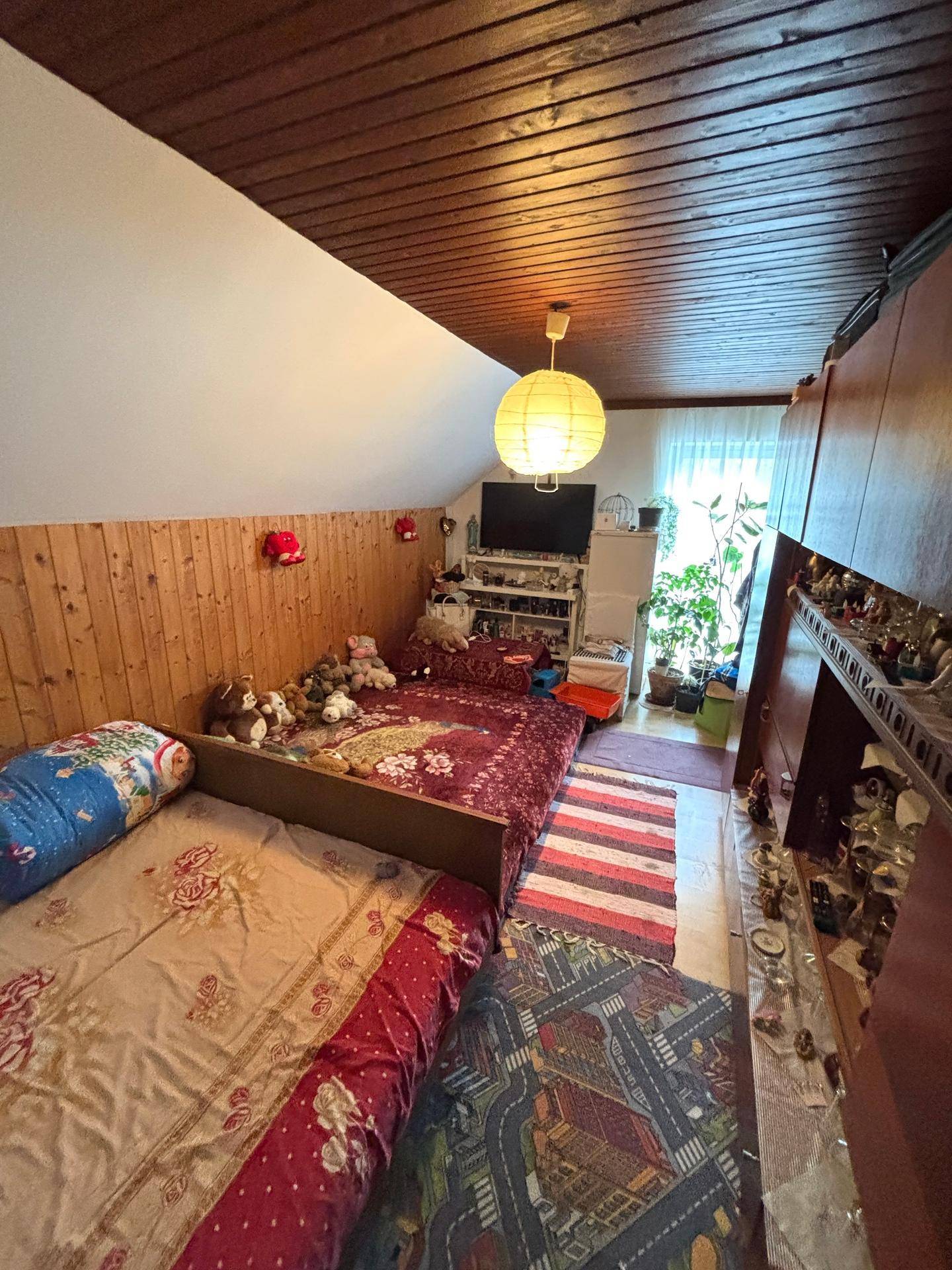 Gemütliches Schlafzimmer im Dachgeschoss mit Holzverkleidung, zwei Betten und schräger Decke.