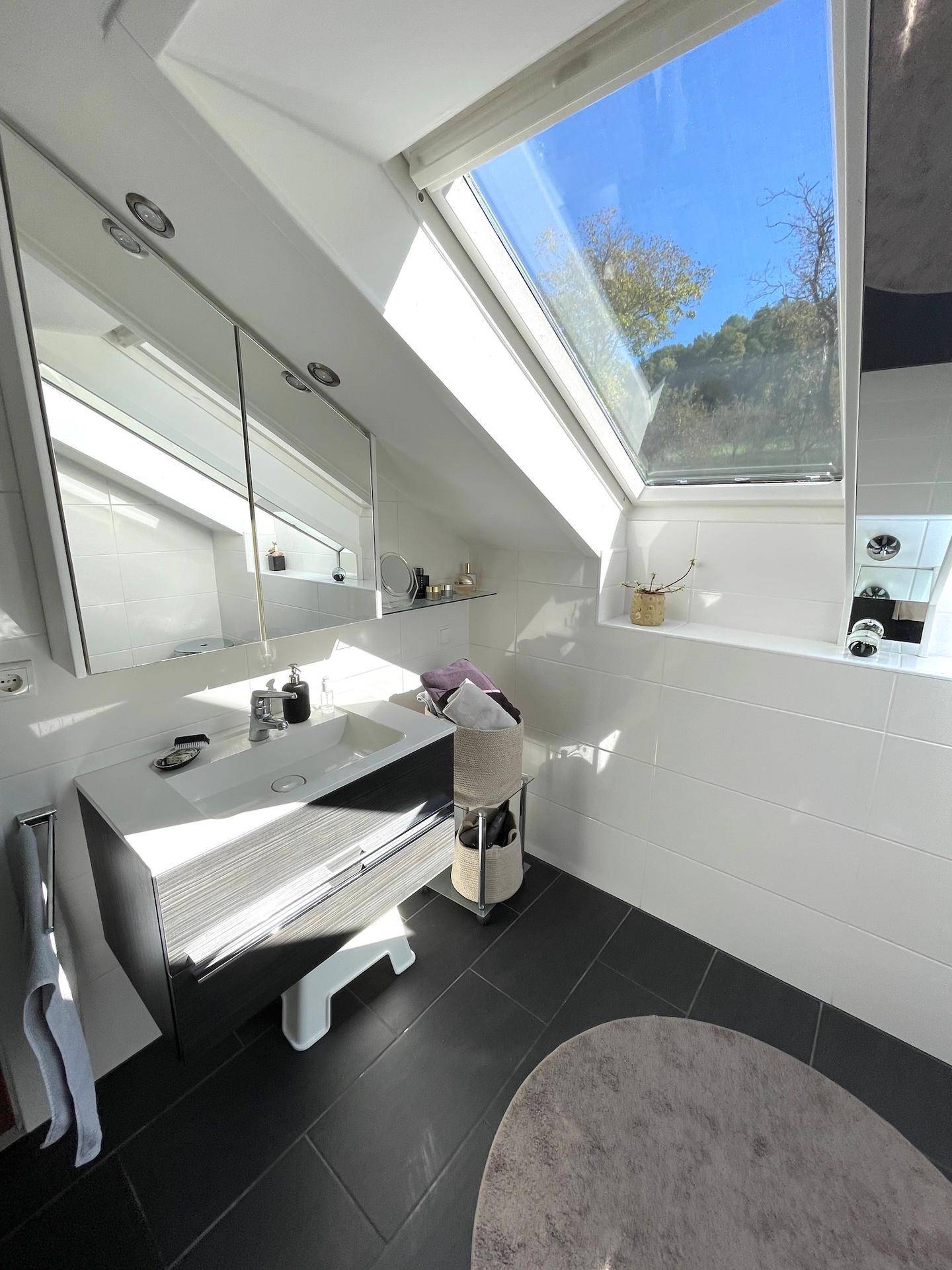 Helles Badezimmer im Dachgeschoss mit modernem Waschtisch, Spiegelschrank und großem Dachfenster.
