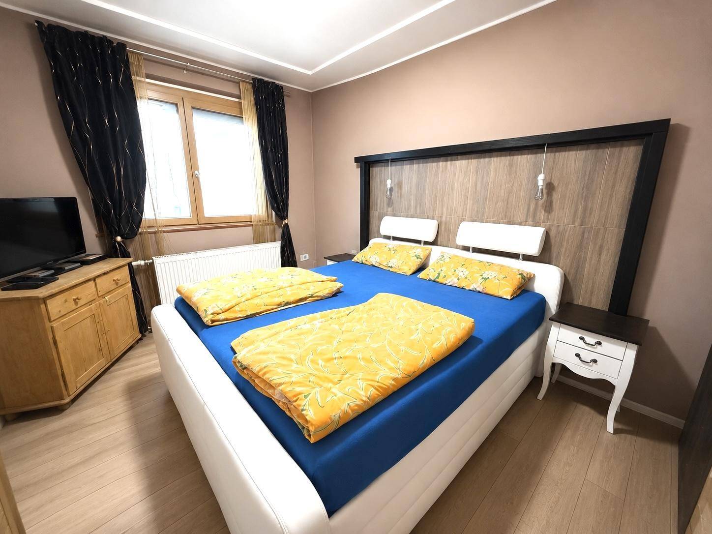 Helles Schlafzimmer mit großem Bett, Fenster und Heizkörper für angenehme Wärme.