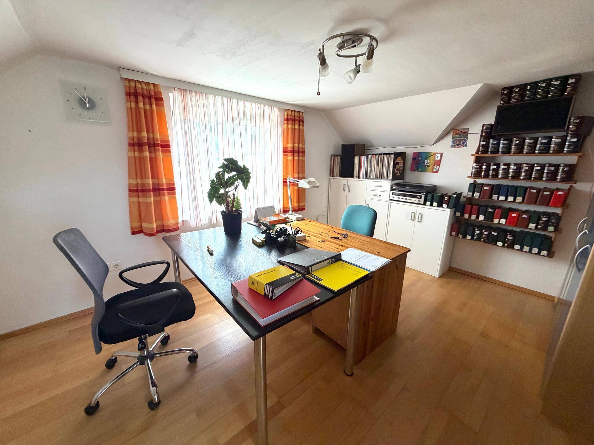 Funktionales Büro mit Schreibtisch, Bürostuhl und Regalen unter der Dachschräge.
