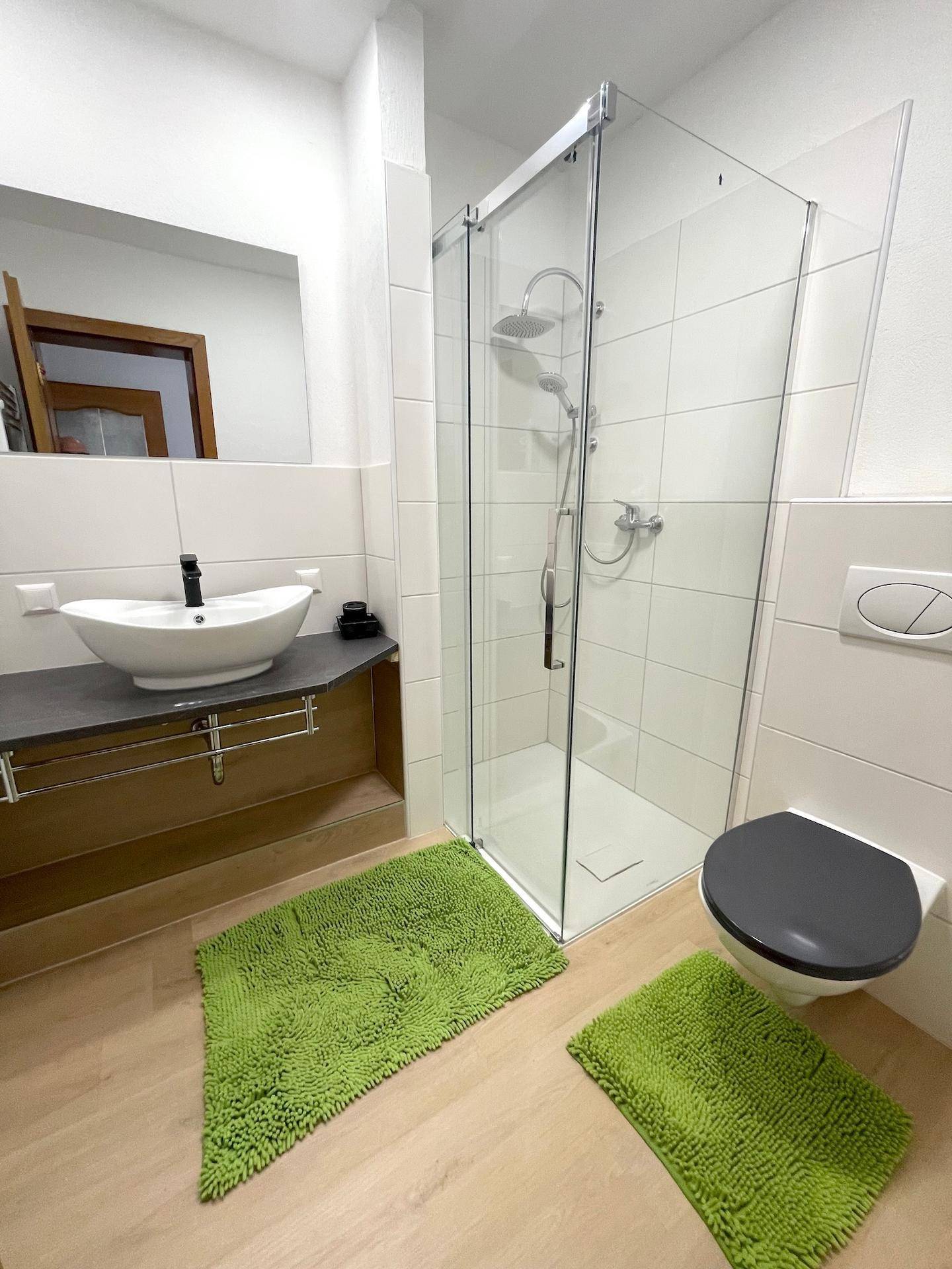 Ein modernes Badezimmer mit begehbarer Dusche, weißen Fliesen und dunklem Boden.