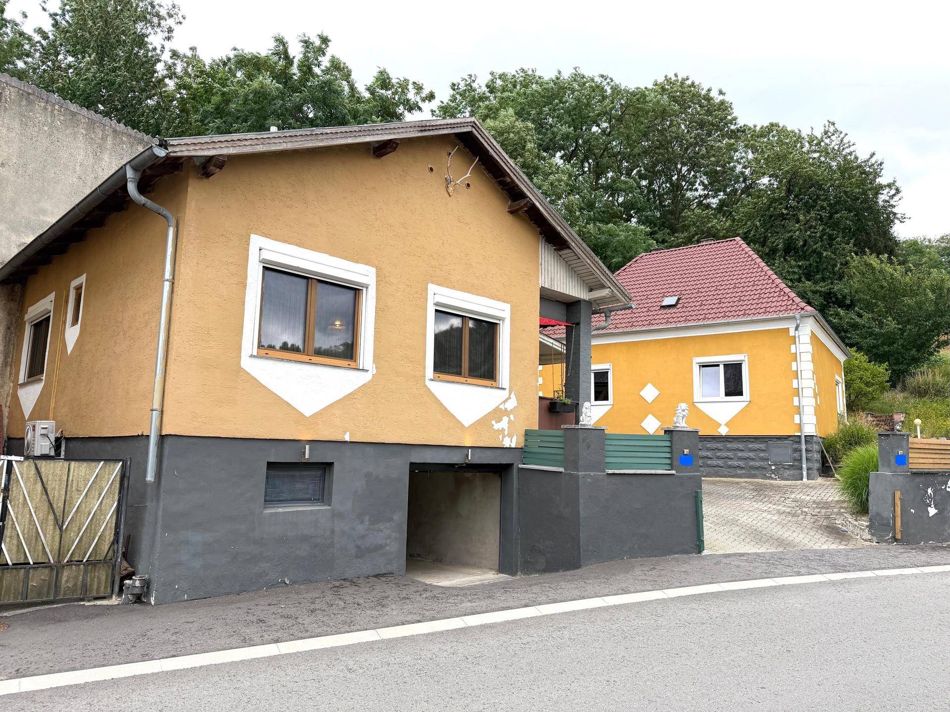 Außenansicht der beiden Häuser von der Straße aus, umgeben von Bäumen.