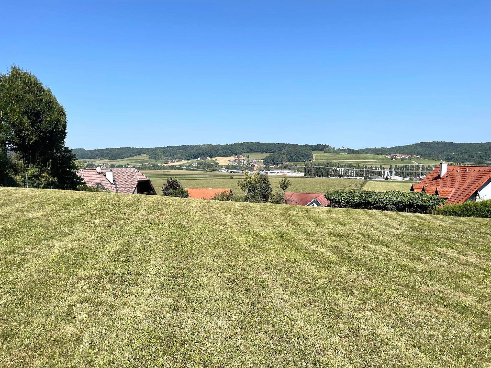 Ausgedehnte Rasenfläche mit Panoramablick auf die hügelige Landschaft und verstreute Häuser in der Ferne.