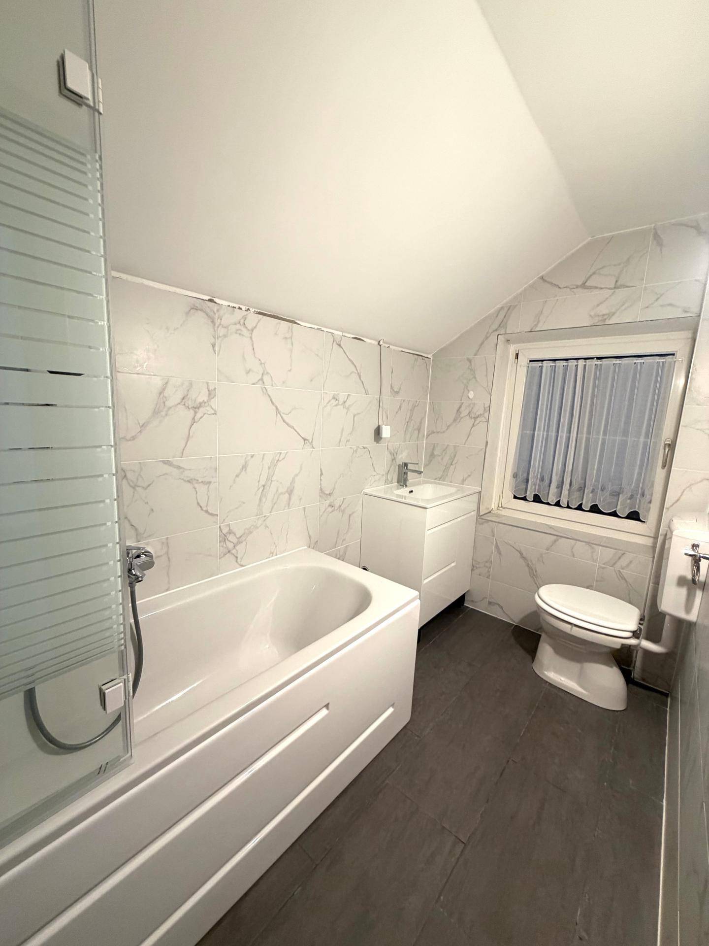 Modernes Badezimmer mit weißen Marmorfliesen, Badewanne mit Duschwand und Fenster.