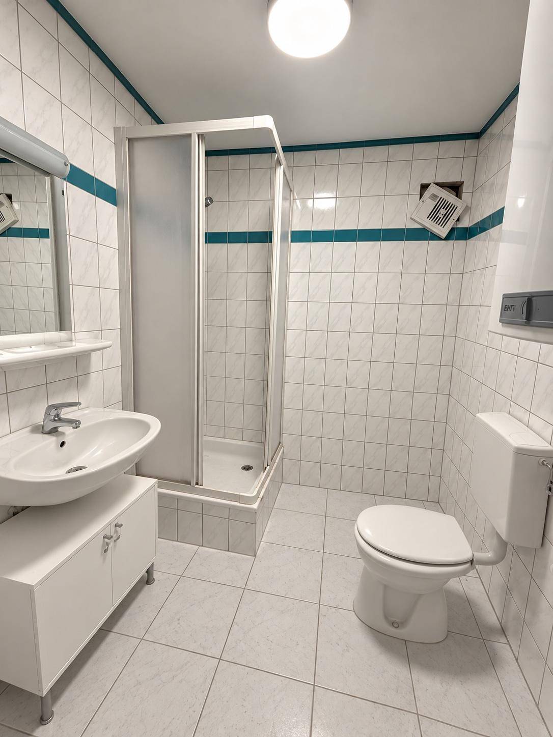 Gefliestes Badezimmer mit Dusche, Waschbecken und WC, ausgestattet mit blauen Akzentfliesen.