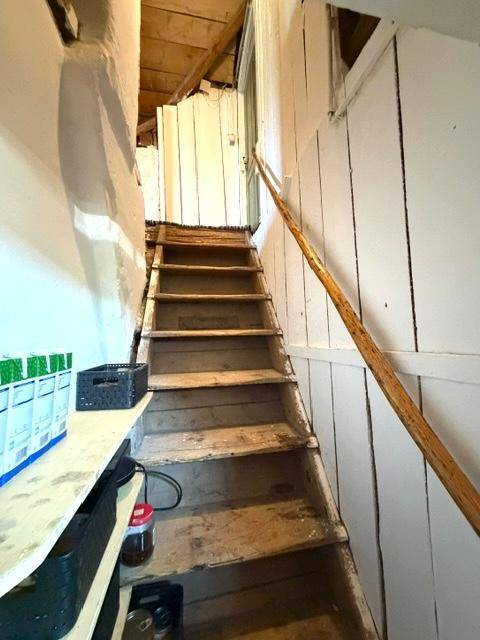 Rustikale Holztreppe führt in einen unfertigen Bereich mit sichtbaren Dachbalken.