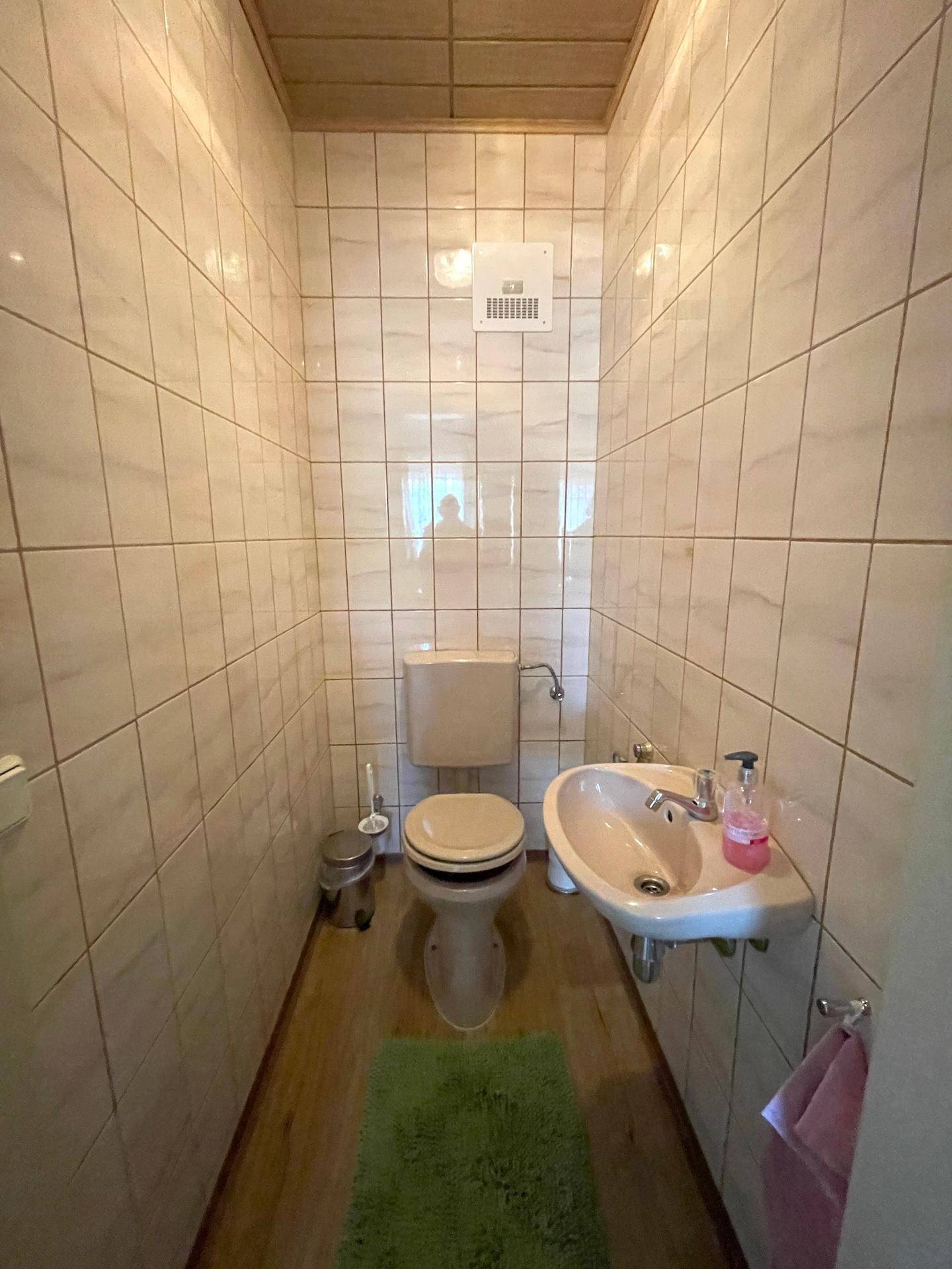 Eine kleine Gästetoilette mit hellen Fliesen, WC und Handwaschbecken.