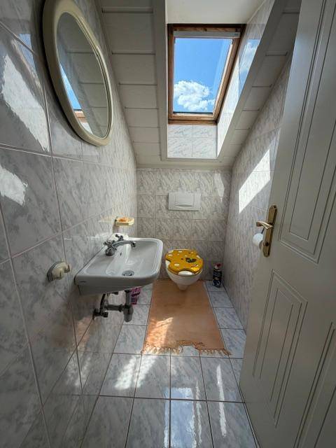 Kleines Gäste-WC mit Dachfenster, gefliesten Wänden und Boden, sowie einem Wand-WC.