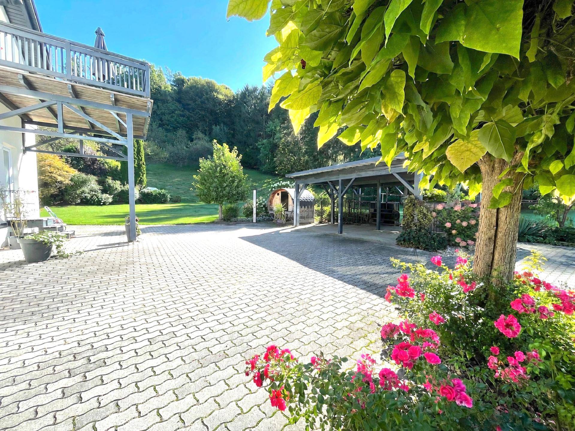 Großer gepflasterter Hof mit Carport, blühenden Rosen und Blick auf das Haus und den Garten.