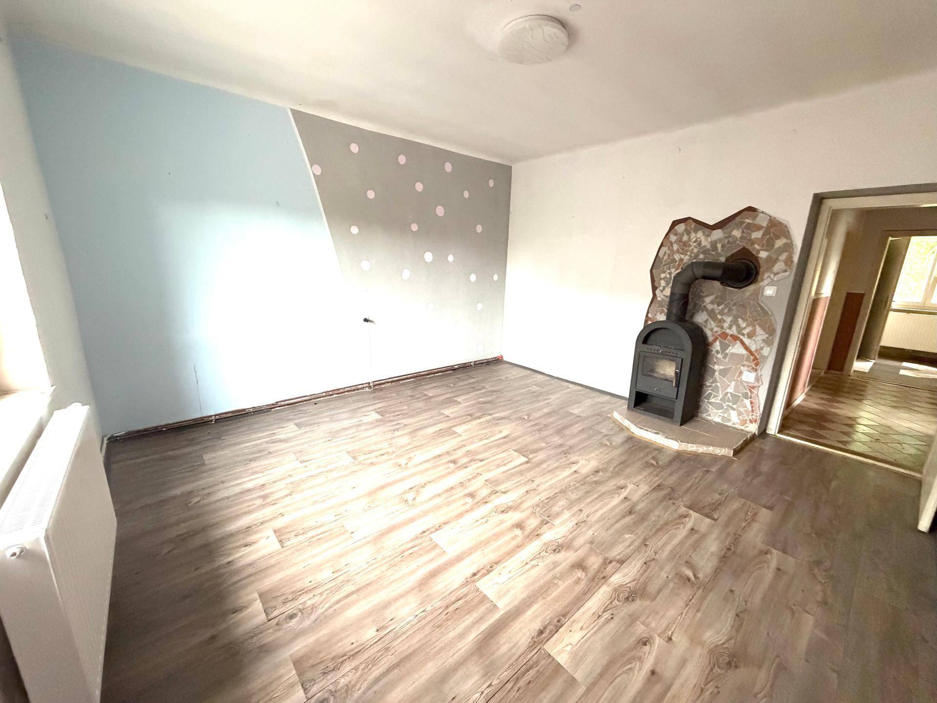 Helles Zimmer mit Kaminofen und Holzboden, teilweise renovierungsbedürftige Wände.