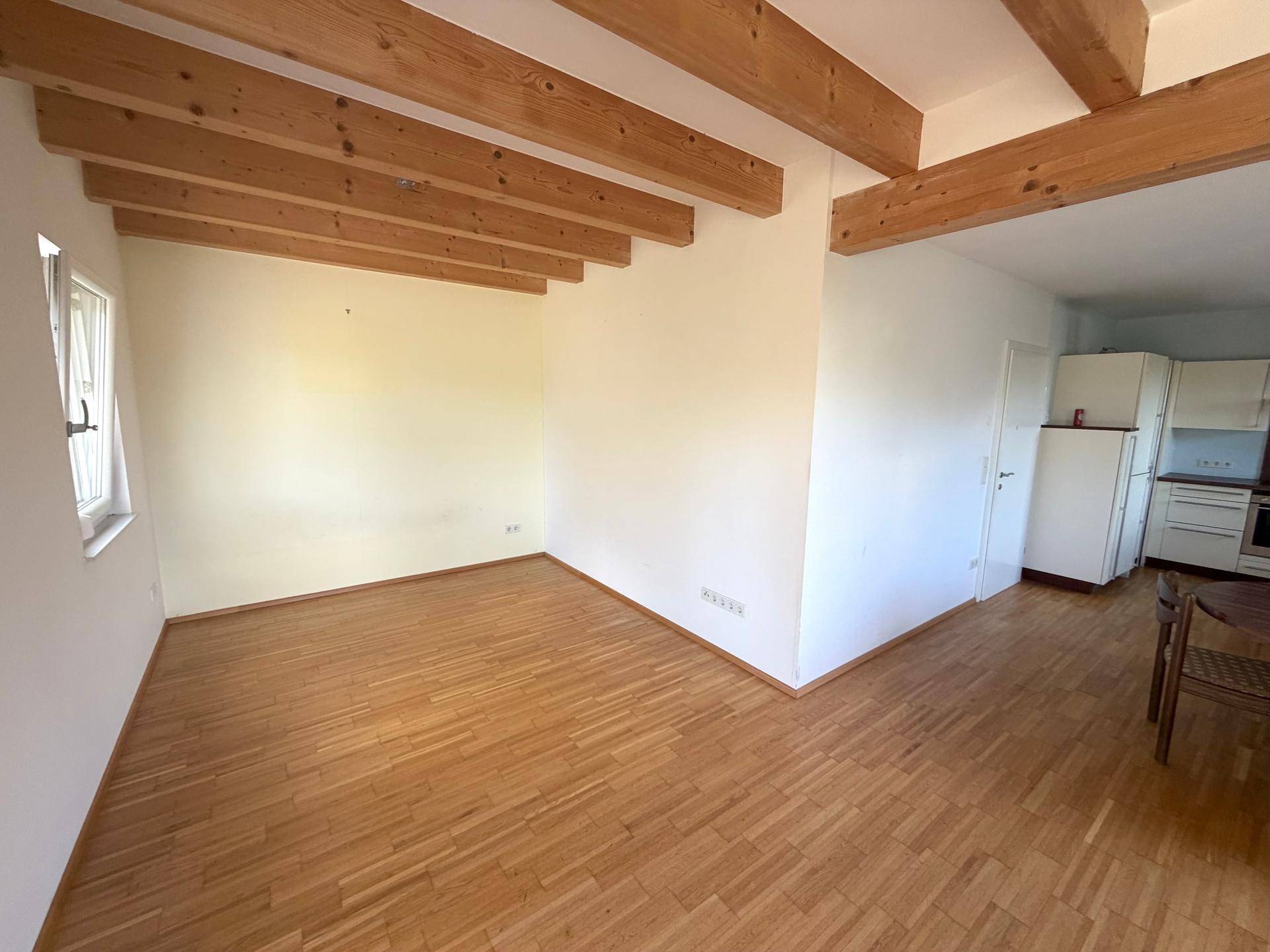 Heller Wohnbereich mit Holzboden und sichtbaren Holzbalken, der viel natürliches Licht erhält.
