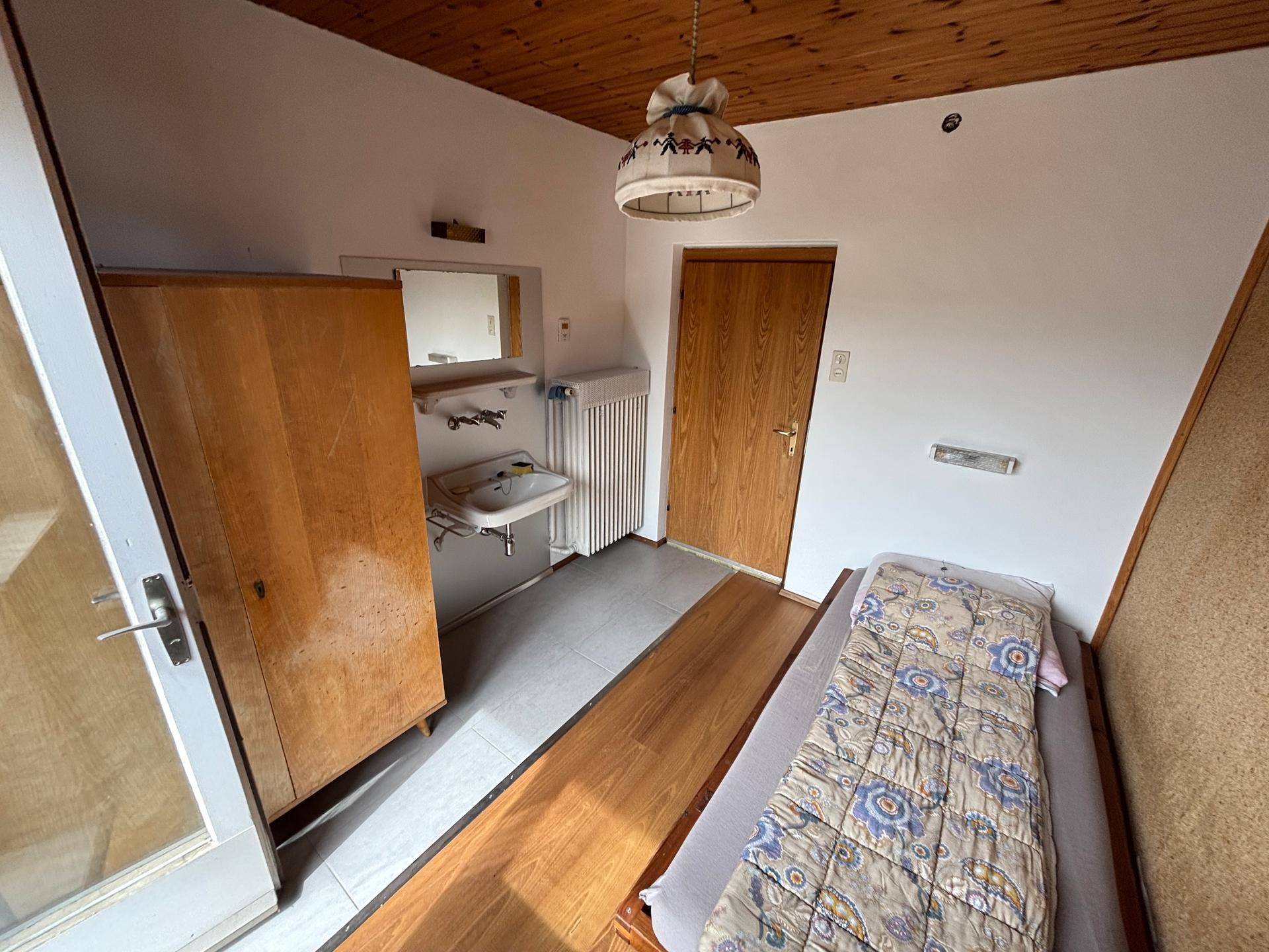 Schlafzimmer mit Korkwänden, Holzboden und integriertem Waschbecken.