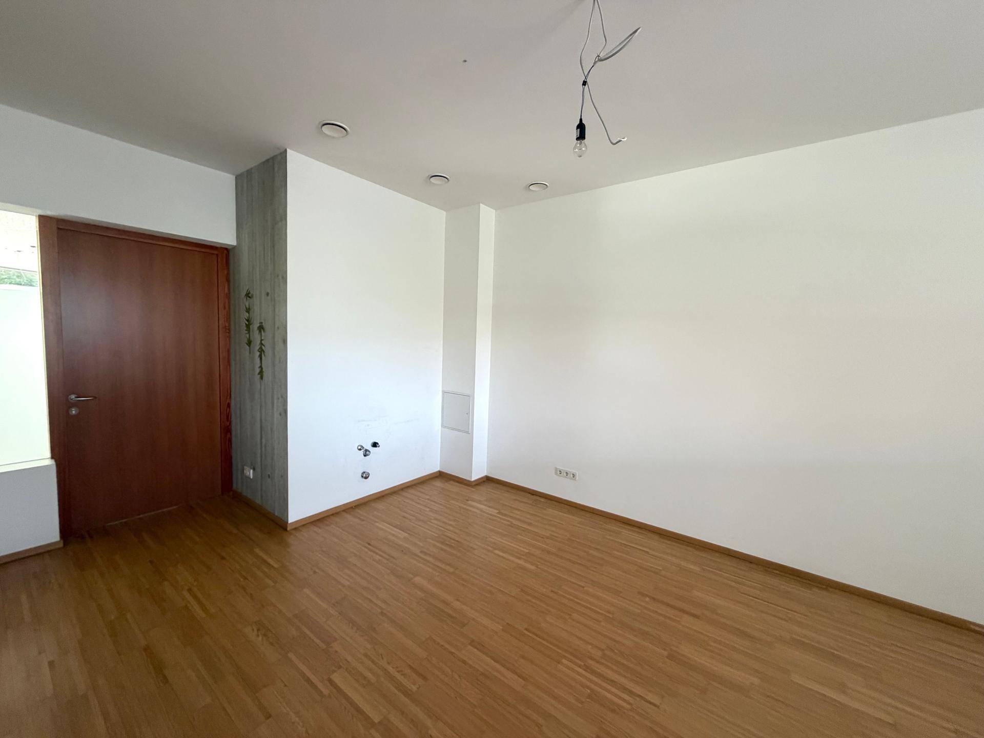 Heller Raum mit Holzfußboden, weißen Wänden und einer Holztür, ergänzt durch eine Betonsäule.
