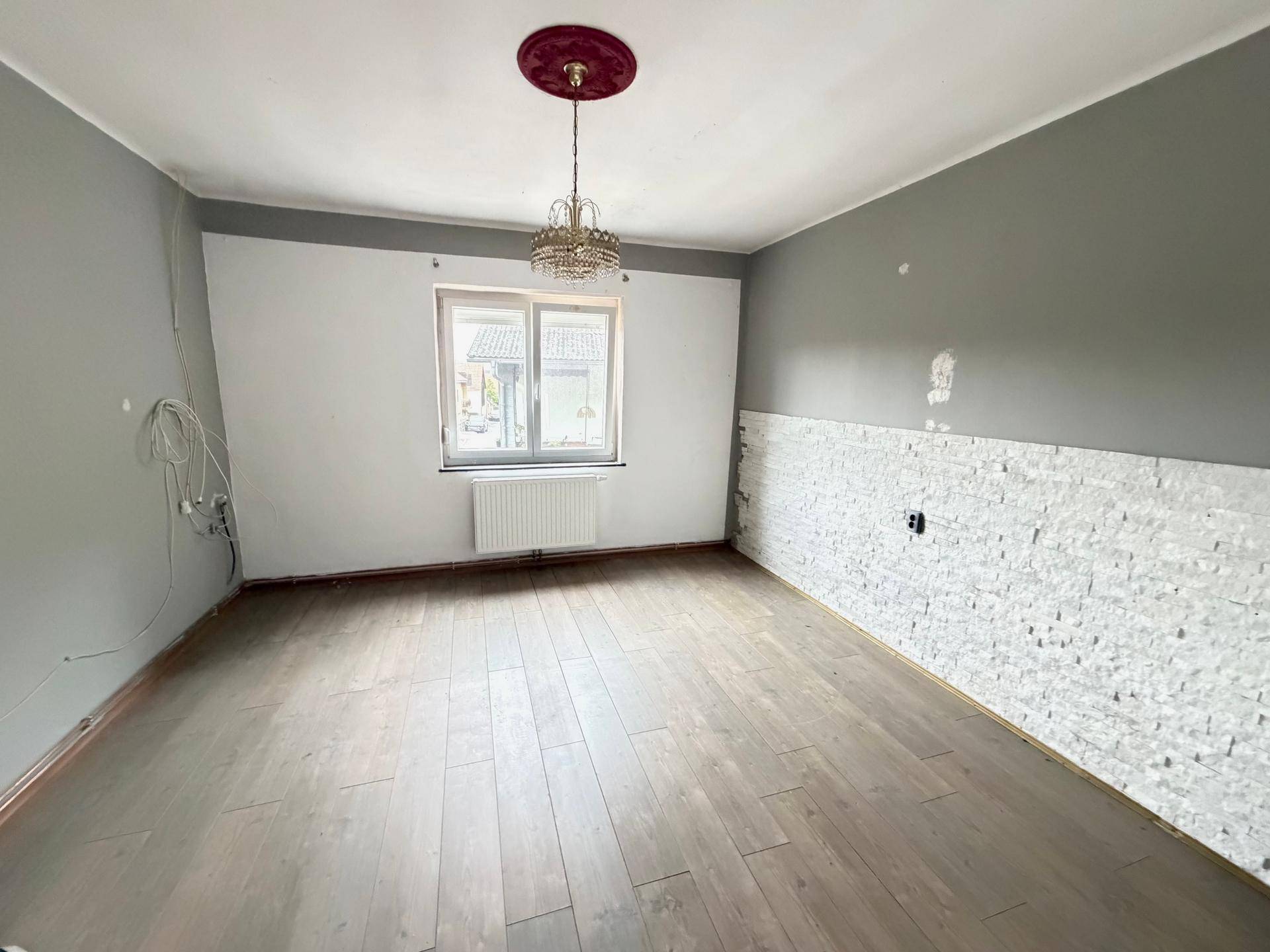 Leeres Schlafzimmer mit Holzboden, Fenster und dekorativer Steinwand, bereit zur Einrichtung.