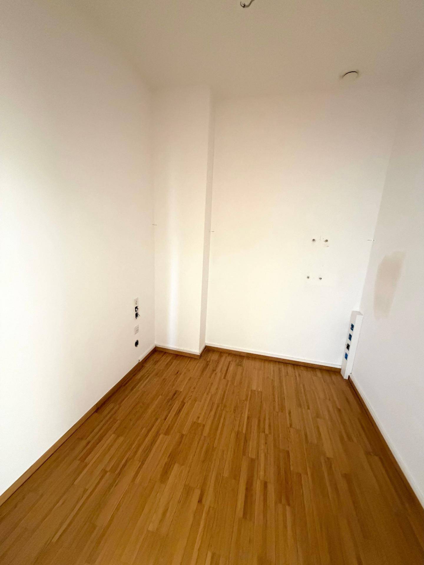 Schmaler Raum mit Holzfußboden und weißen Wänden, vorbereitet für elektrische Installationen.
