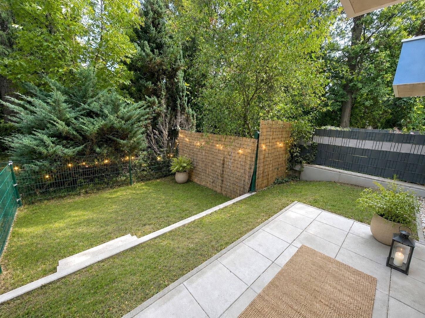 Gepflegter Gartenbereich mit Rasenfläche, Terrasse und dekorativer Beleuchtung entlang des Zauns.
