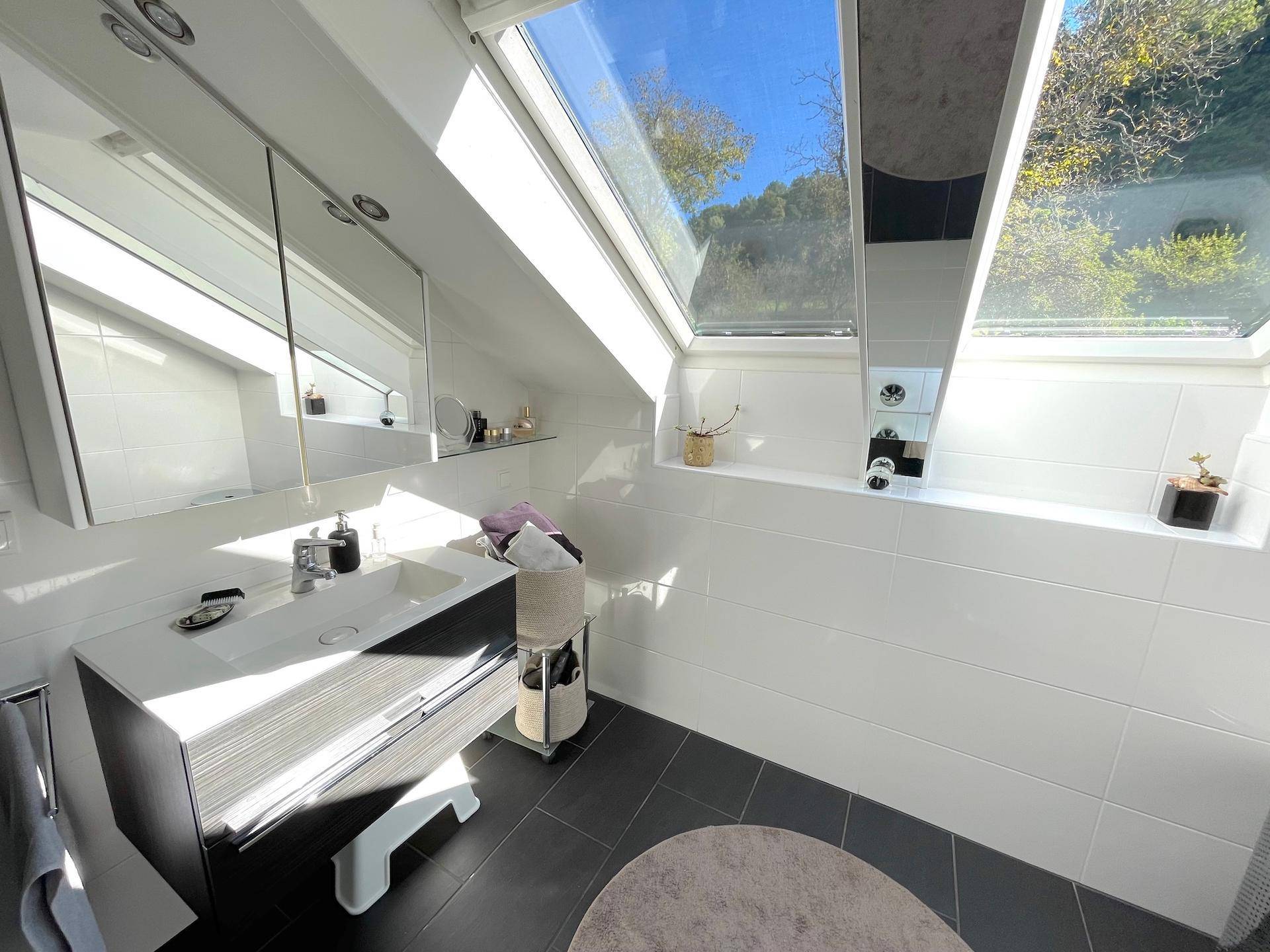 Helles Badezimmer im Dachgeschoss mit modernem Waschtisch, Spiegelschrank und Dachfenstern.