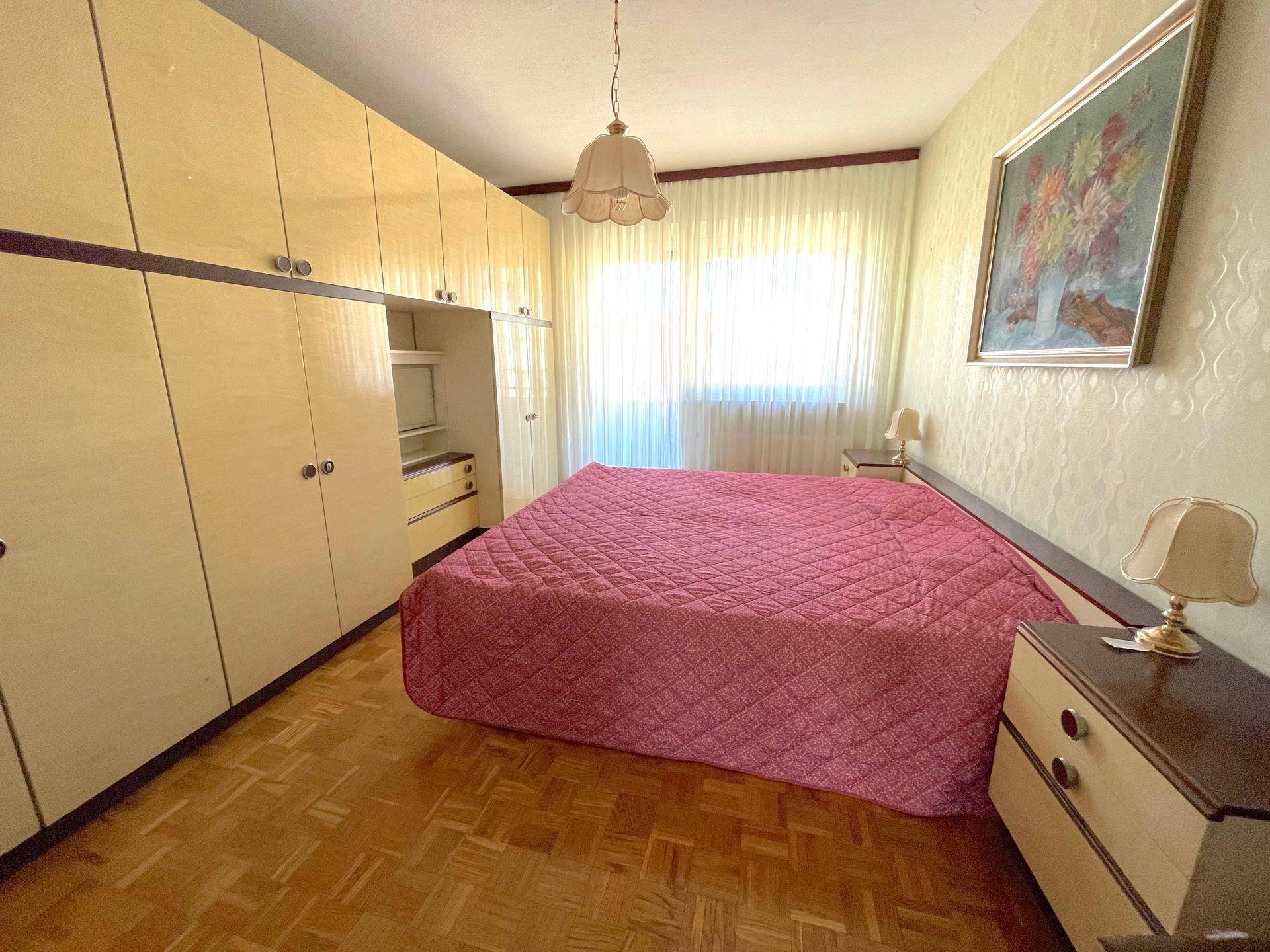 Schlafzimmer mit Doppelbett, Einbauschränken und Parkettboden, hell durch großes Fenster.