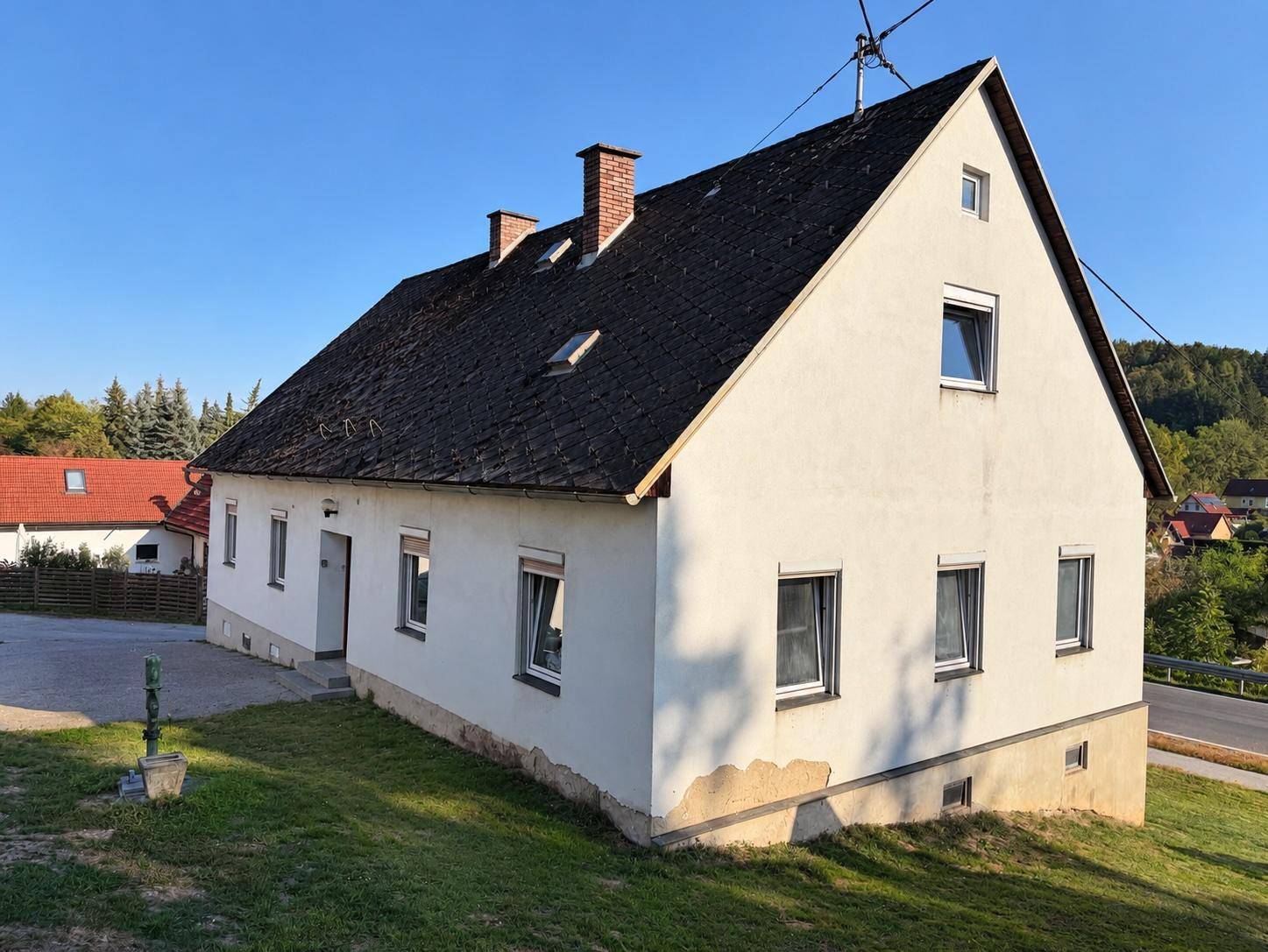 Freistehendes Haus mit weißer Fassade, Satteldach und Schornsteinen.