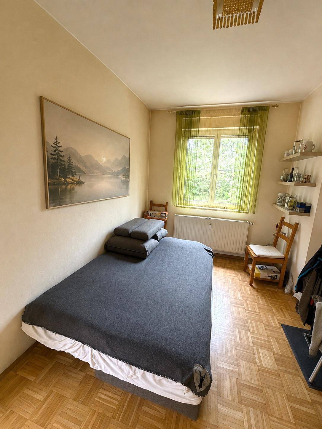 Gemütliches Schlafzimmer mit Parkettboden, großem Fenster und Blick ins Grüne.