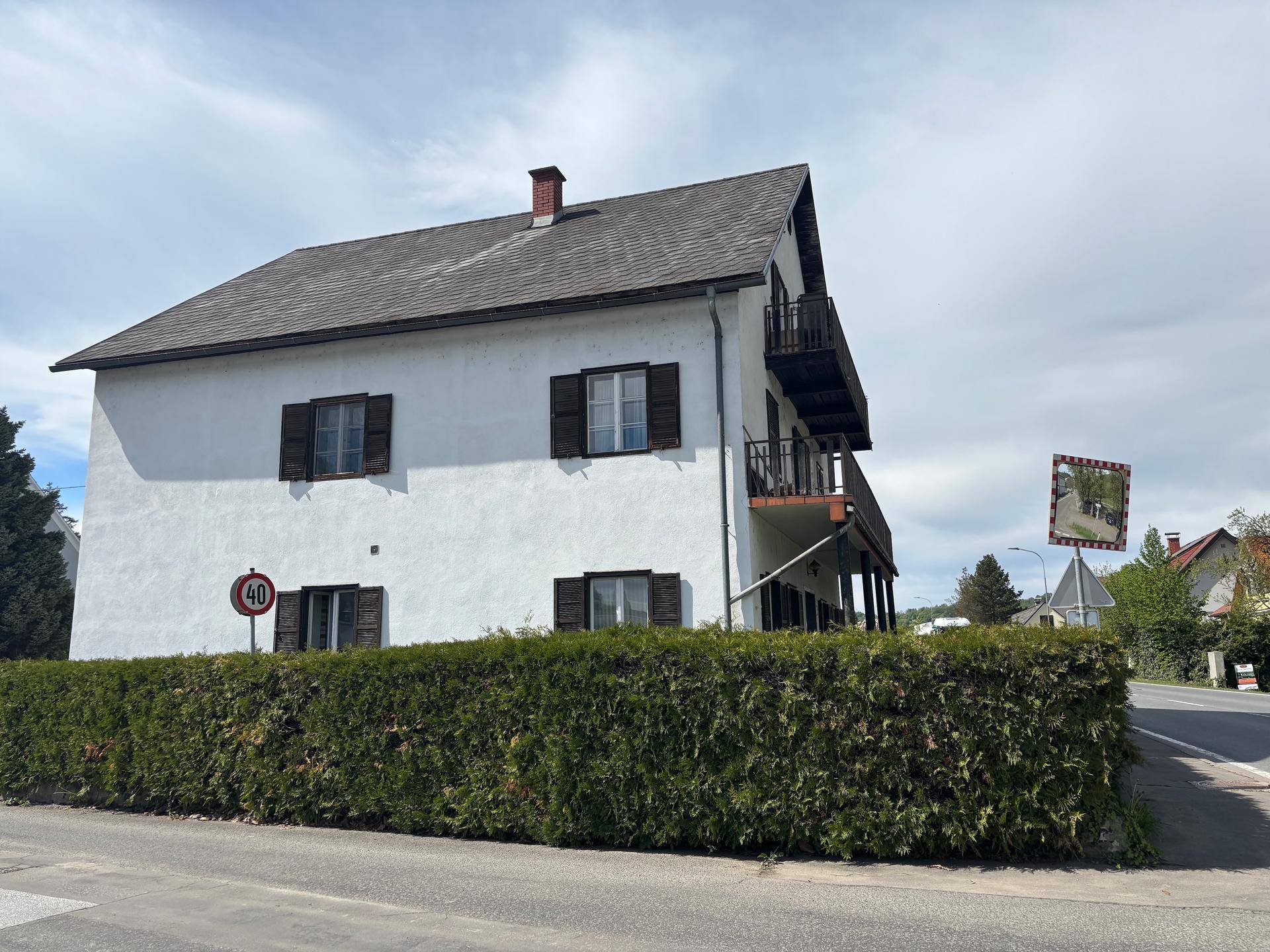Ansicht des Wohnhauses von der Straße mit einer hohen Hecke und Balkonen.