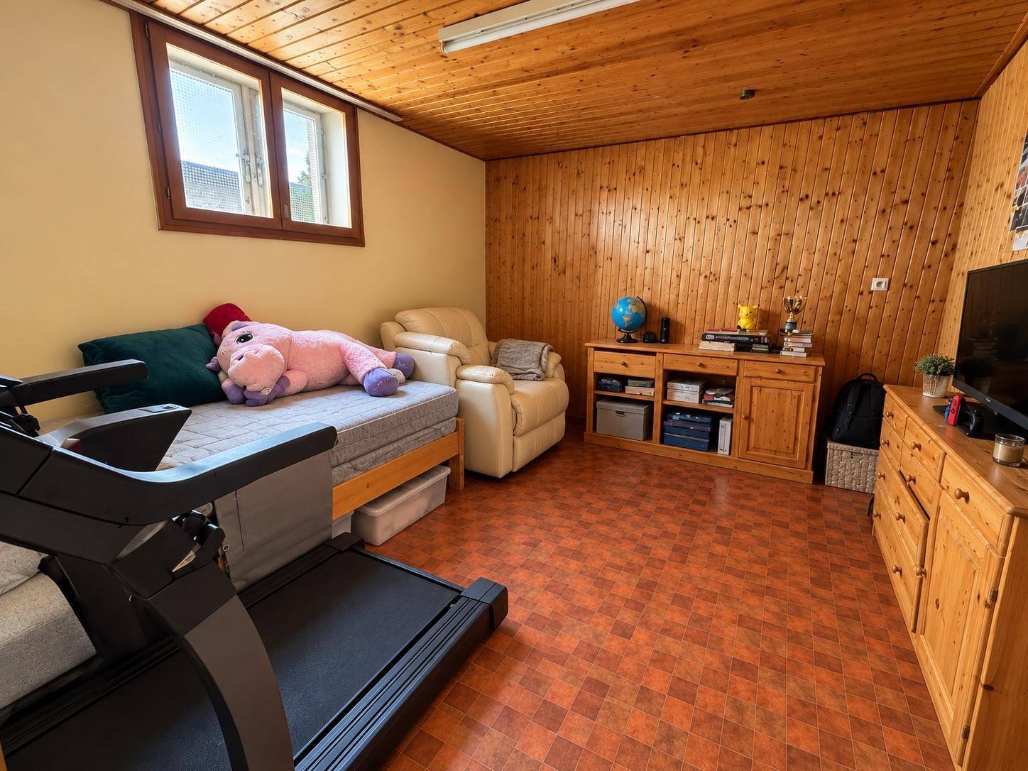 Ausgebauter Kellerraum mit Holzvertäfelung, Bett und Unterhaltungselektronik, gemütlich eingerichtet.
