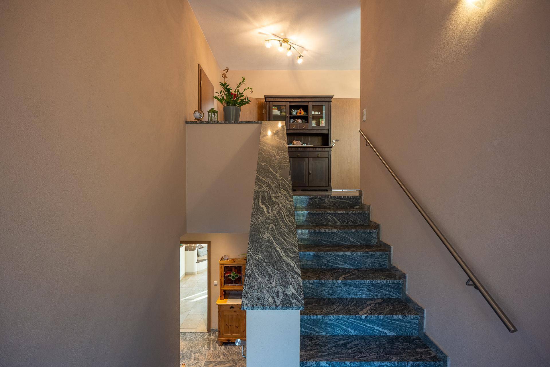 Treppenhaus mit elegantem Marmorboden und Holzgeländer, das die Etagen verbindet.