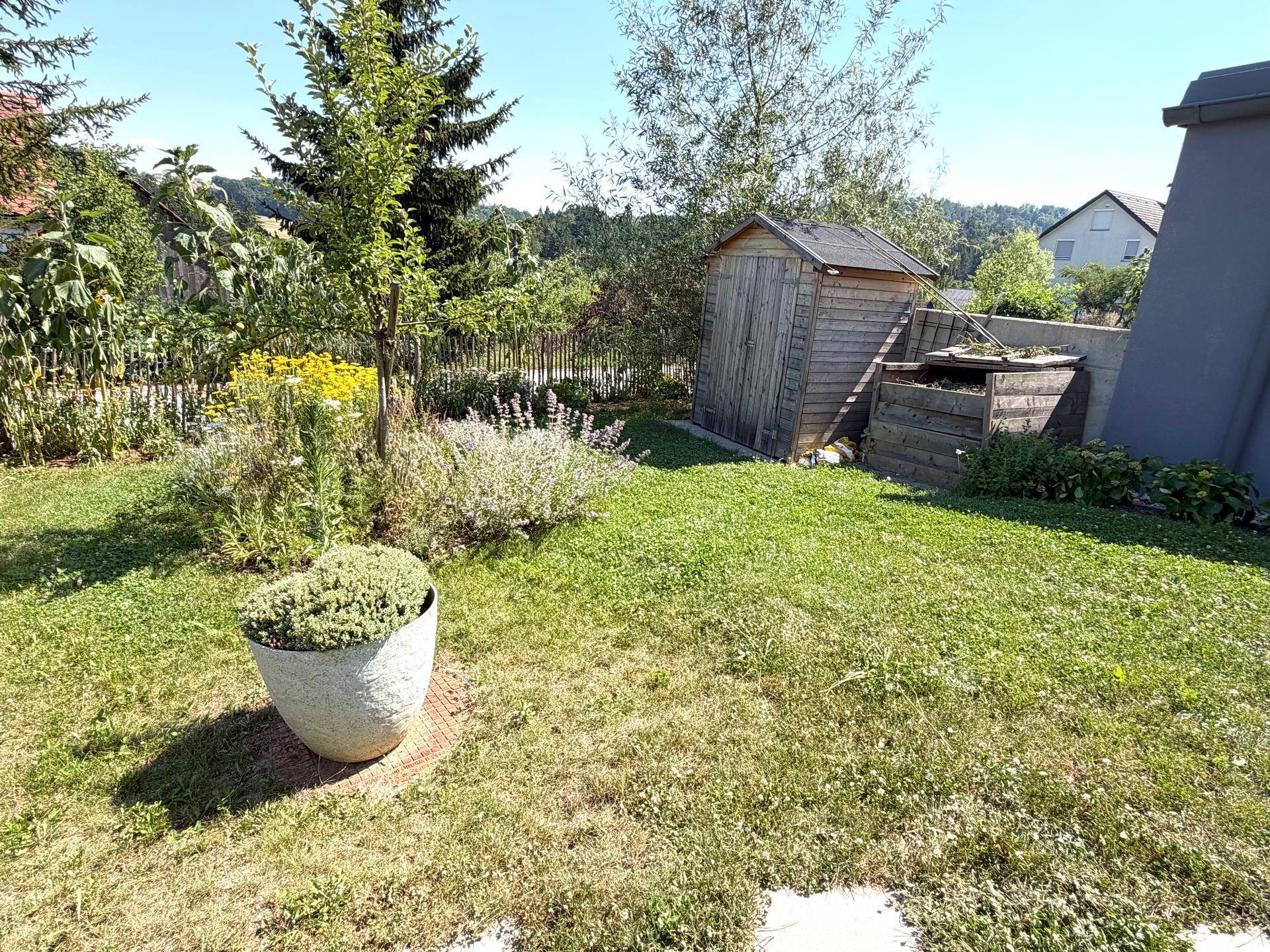 Gepflegter Garten mit vielfältiger Bepflanzung, Rasenfläche und praktischem Geräteschuppen.