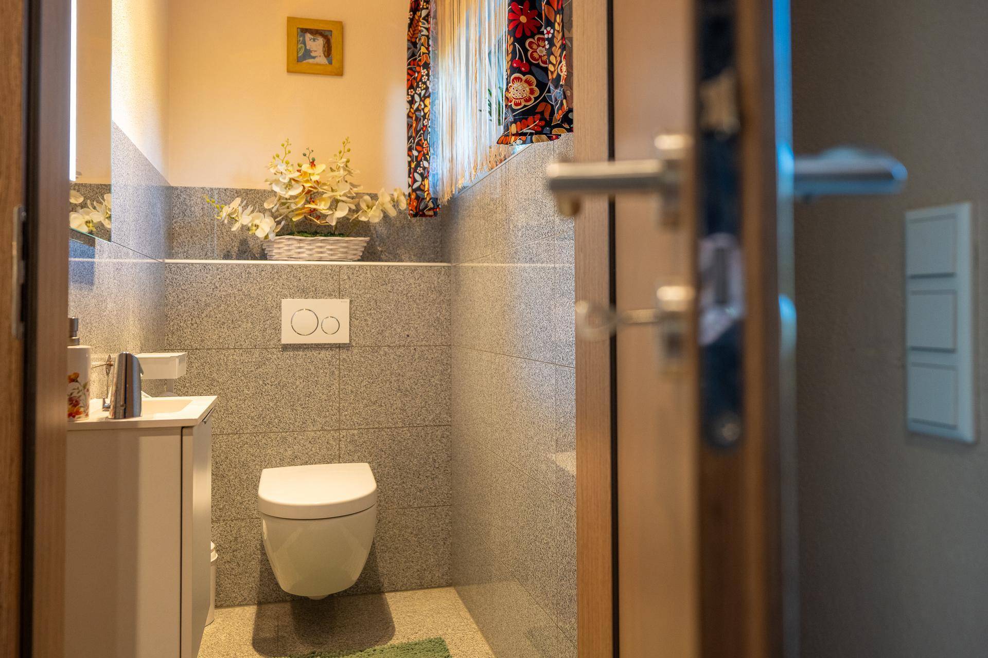 Modernes Gäste-WC mit Wand-WC, kleinem Waschbecken und grauen Fliesen.